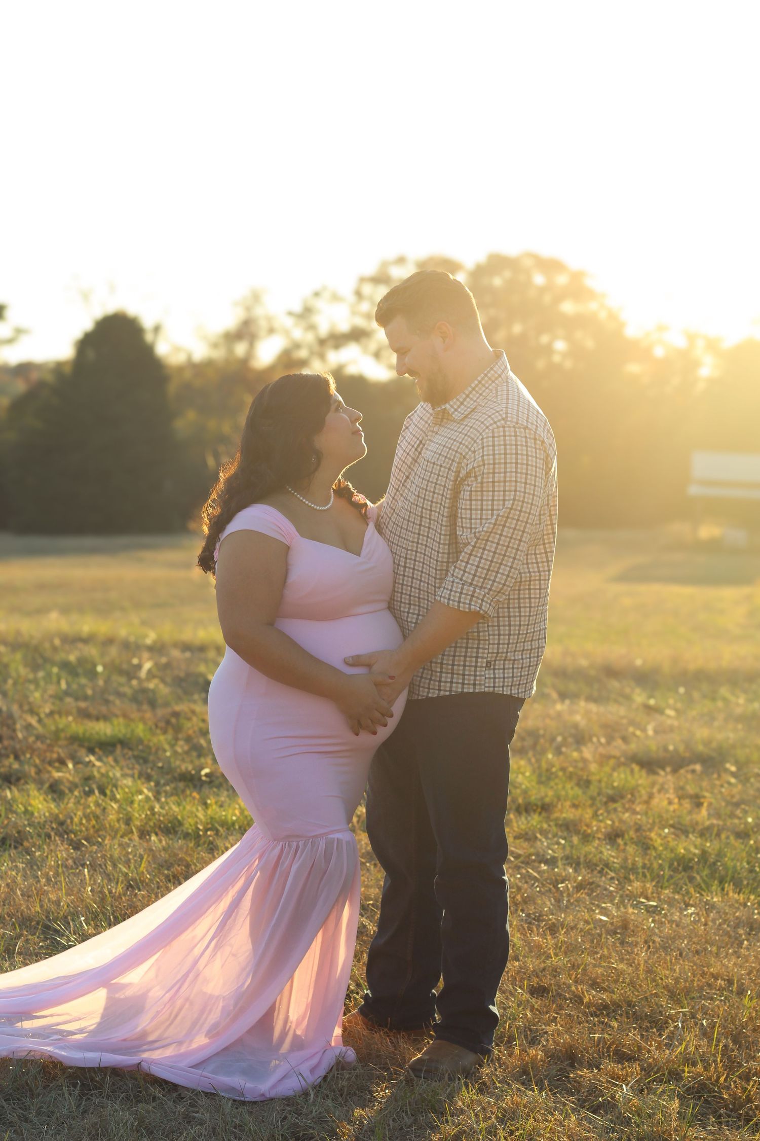 Romantic sunset maternity photos of couple in field with golden light.