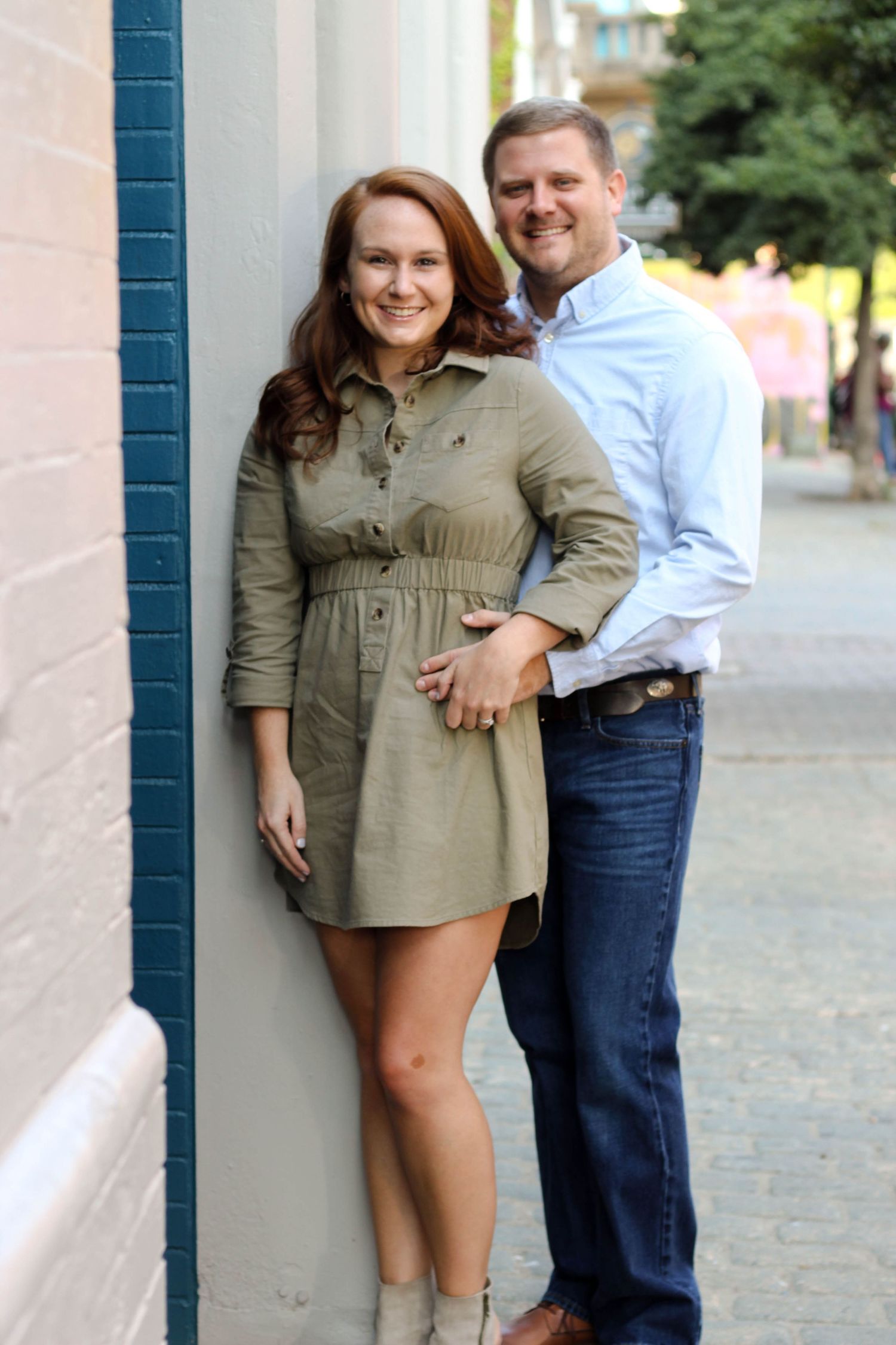A couple poses playfully together against an urban backdrop with white walls.