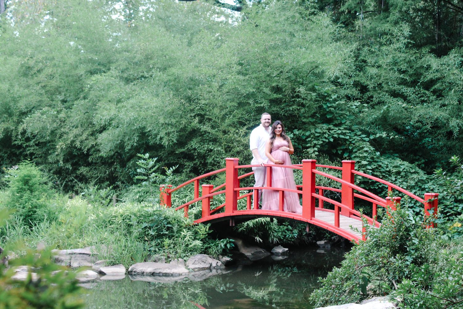Red oriental bridge creates striking contrast against green garden foliage.