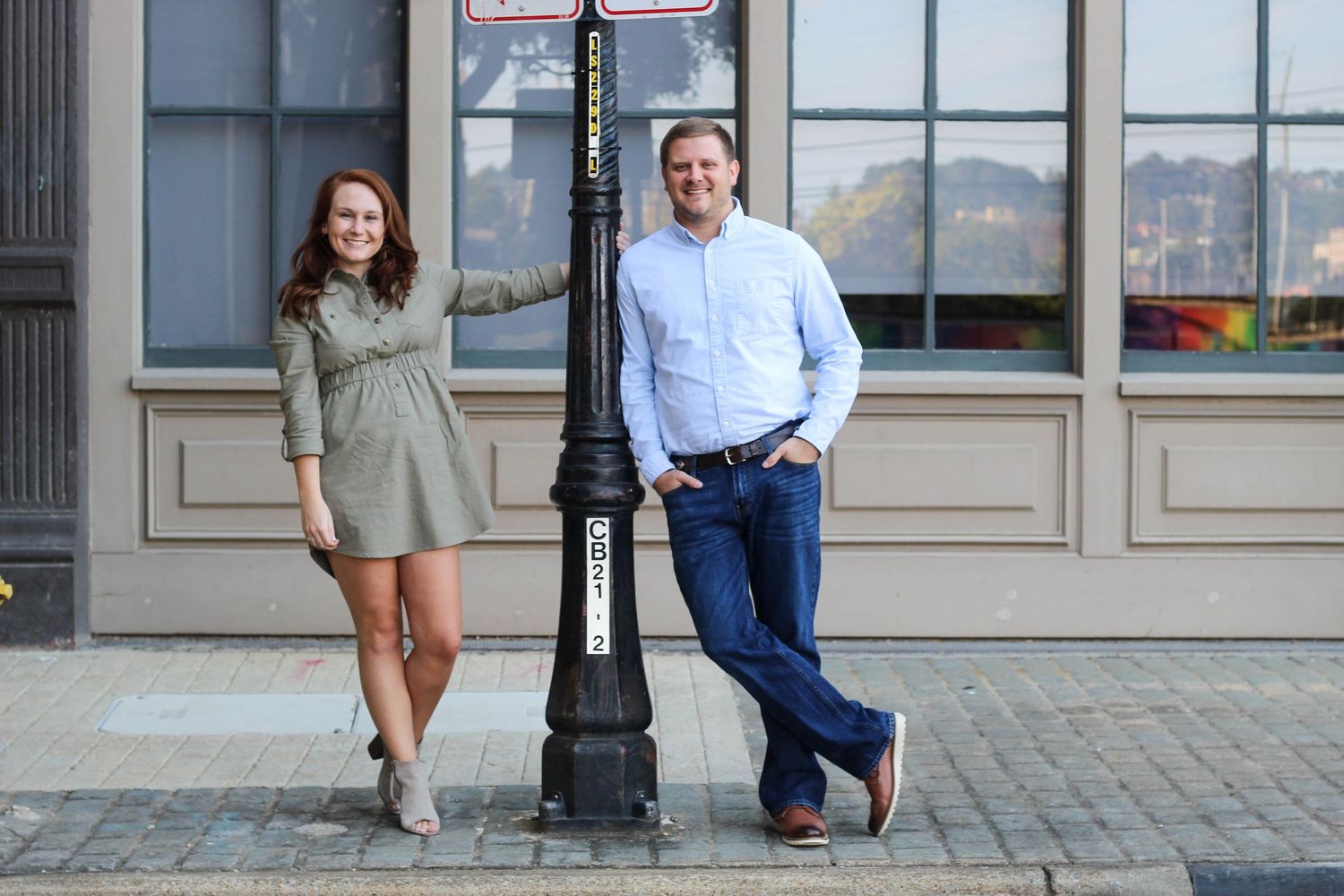 Couple poses casually against brick building exterior.