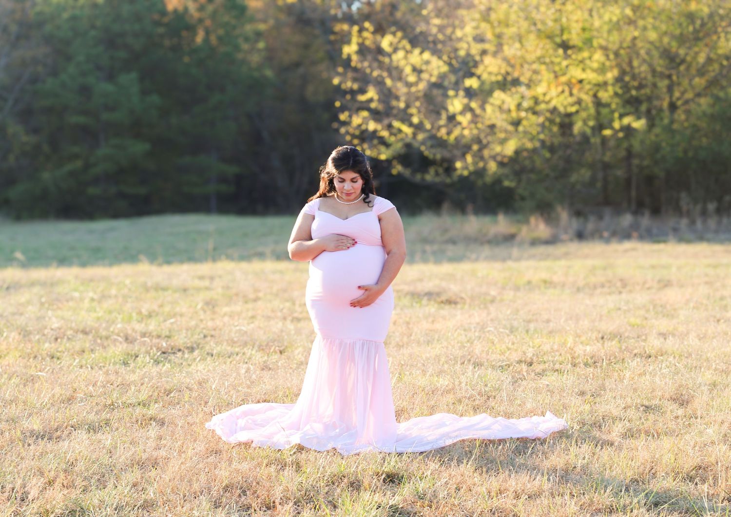 Ethereal maternity portraits in pink gown against golden sunset backdrop.