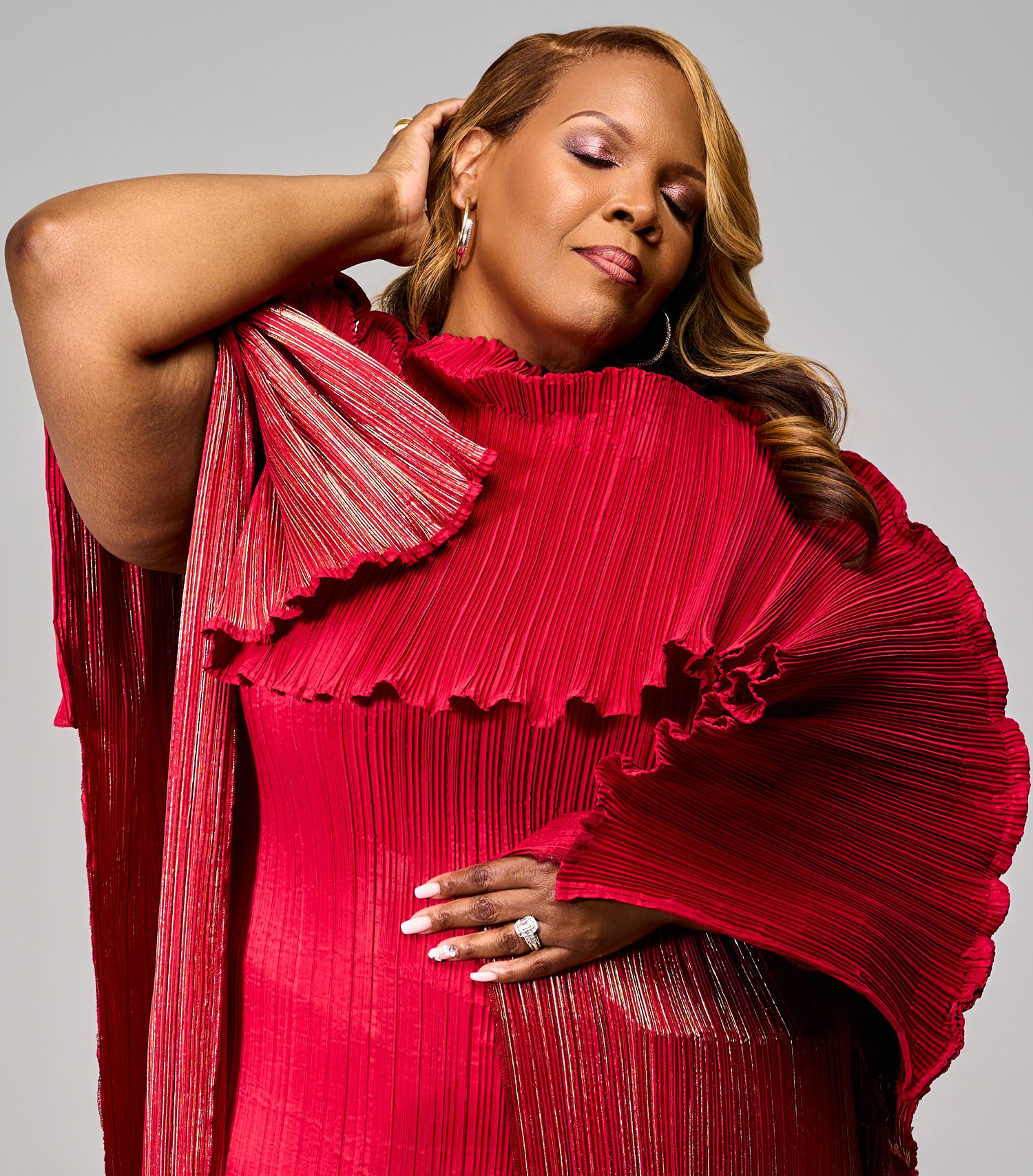Person wearing dramatic red pleated dress poses elegantly against grey studio backdrop.