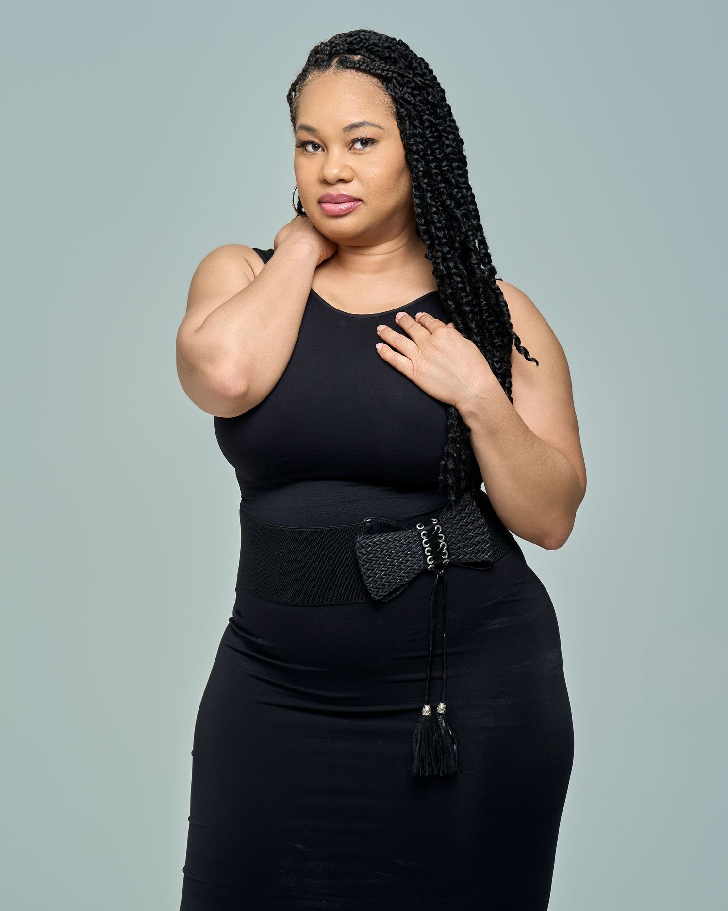 Model in black sleeveless dress poses confidently against gray background in four different poses.