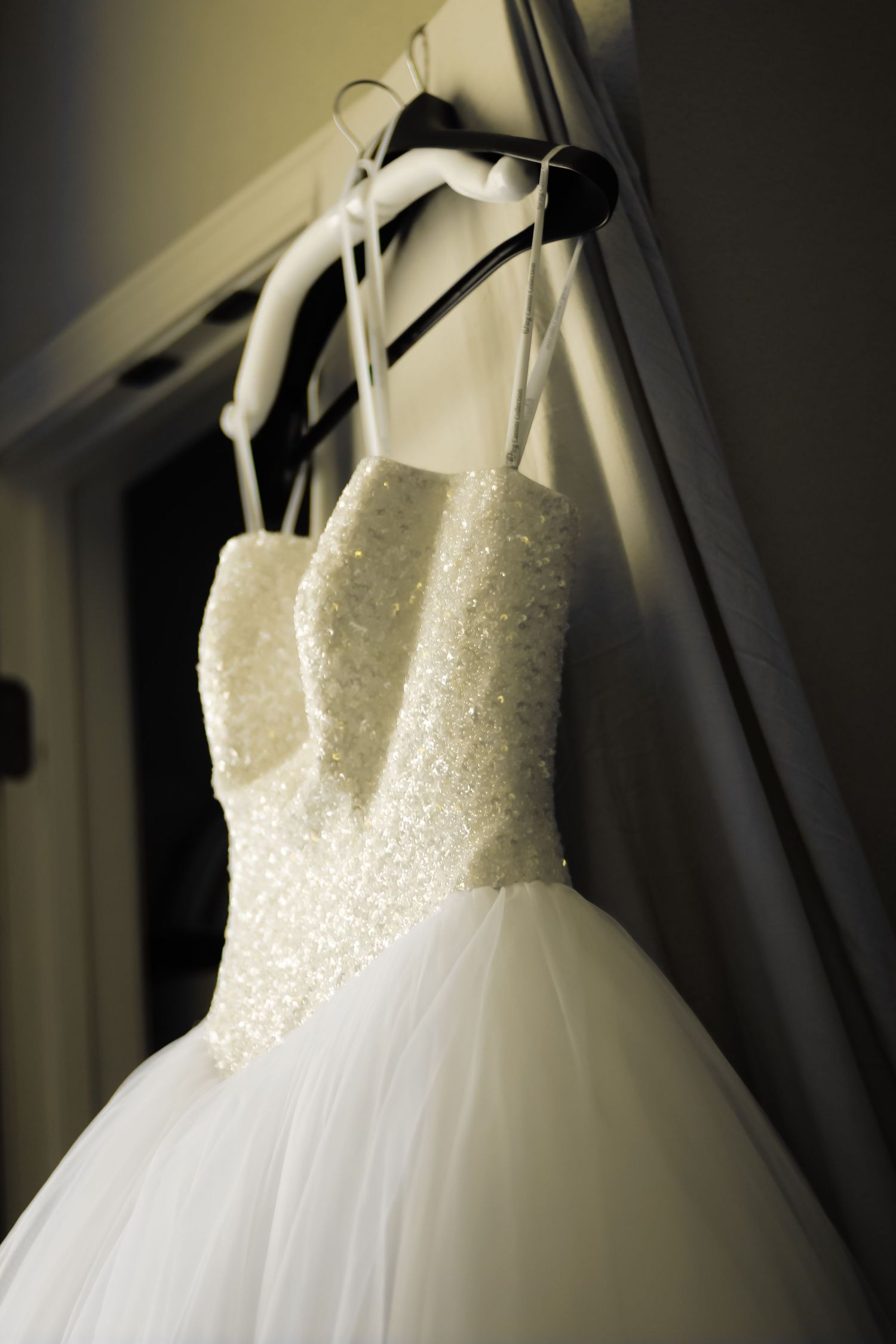 Close-up views of a white beaded wedding dress bodice and tulle skirt hanging on display from different angles.