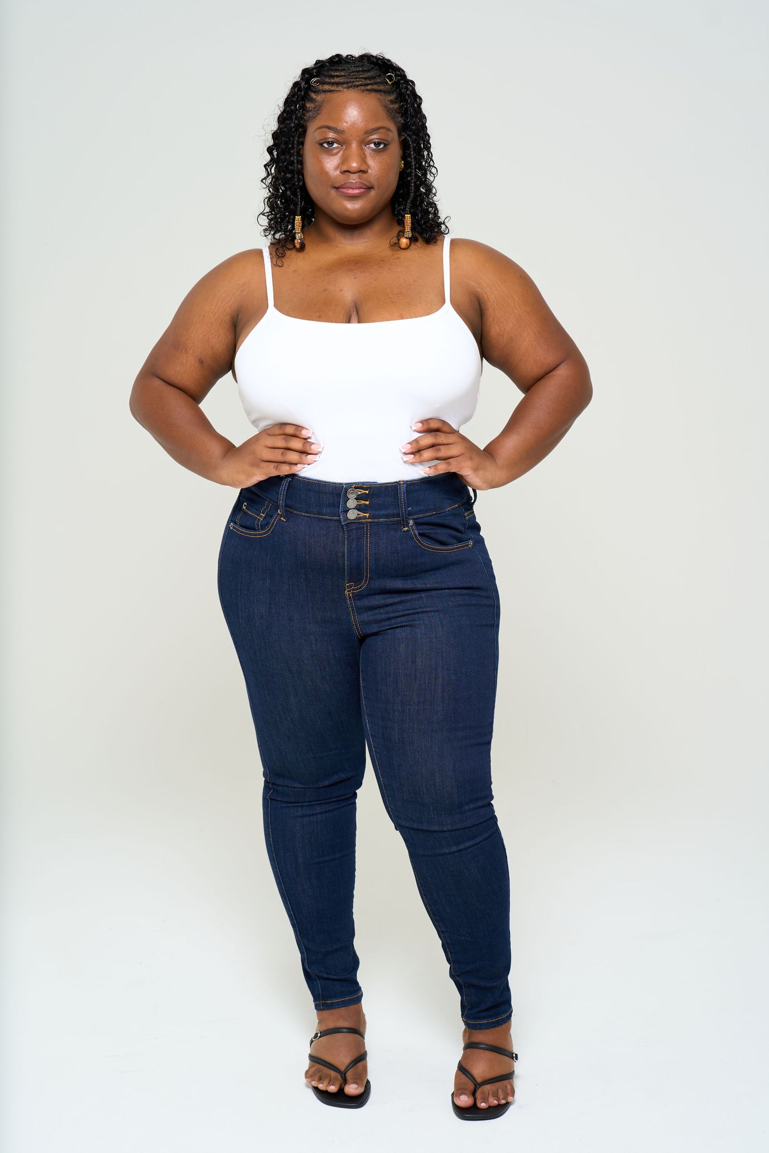 Person wearing a white tank top and dark blue jeans poses in three different angles against a light background.