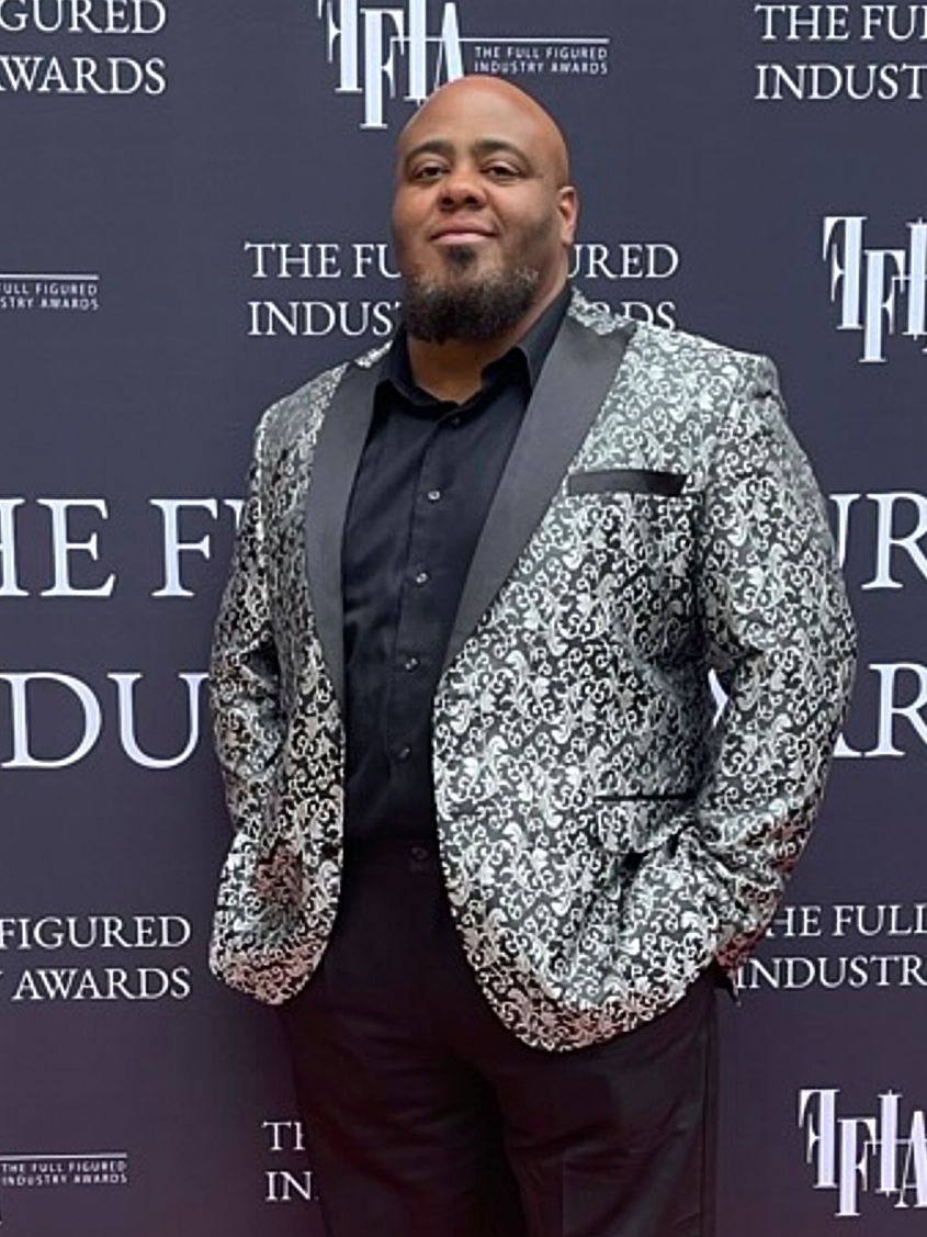 A person in a sparkly silver sequined blazer poses against a dark backdrop with repeating event logo text.