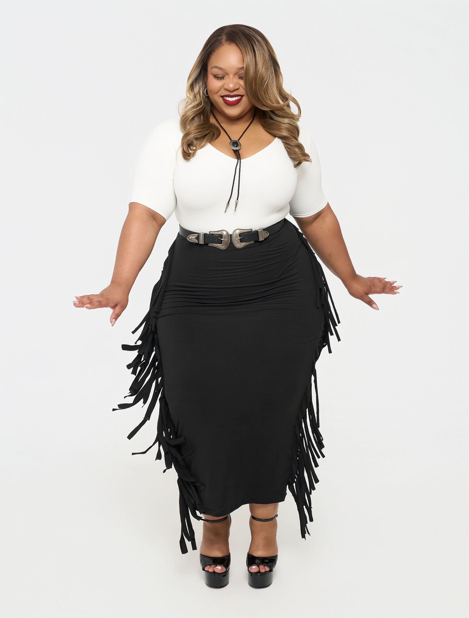 A plus size model in a white top and black fringe skirt poses playfully in a fashion photoshoot series.