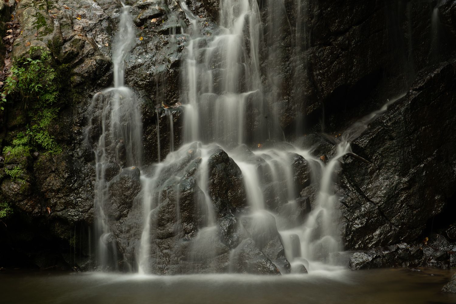 Long exposure photograph of cascading waterfall flowing over dark rocky cliff.