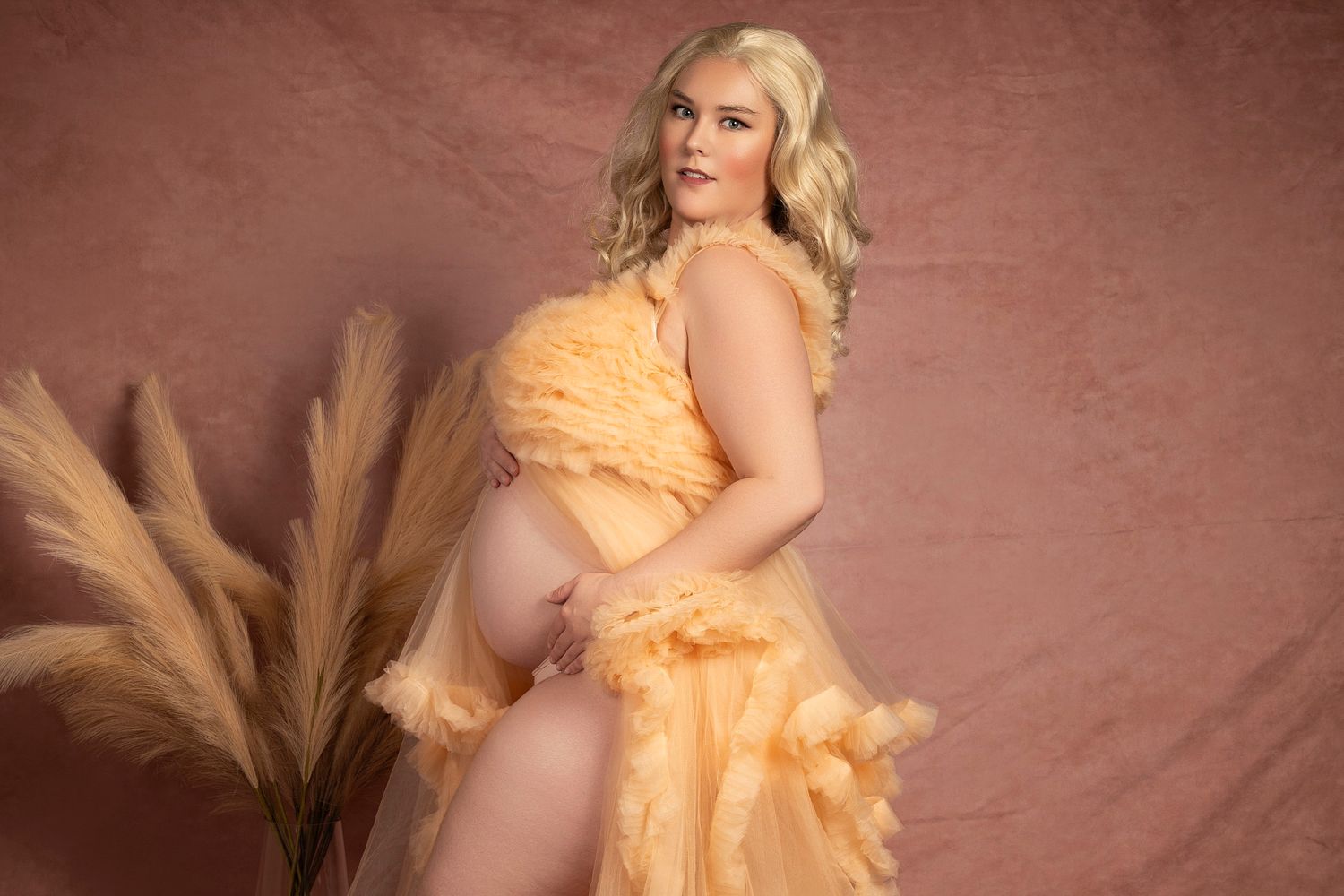 Model in peach ruffled dress poses artistically against textured mauve backdrop.