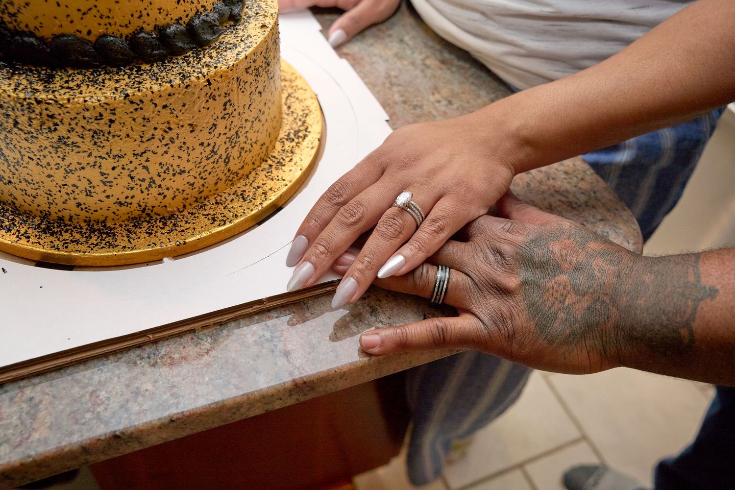 A hand sprinkles poppy seeds onto a large round baking sheet covered in dough in a commercial kitchen setting.