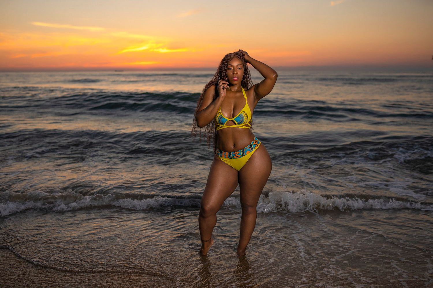 Person in yellow swimsuit poses joyfully on beach during golden sunset.