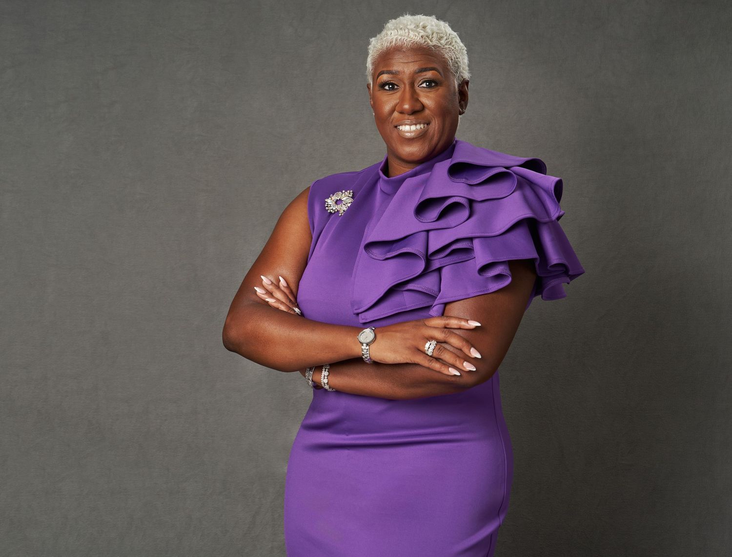 Elegant studio portrait in a form-fitting purple dress with ruffled shoulder detail.