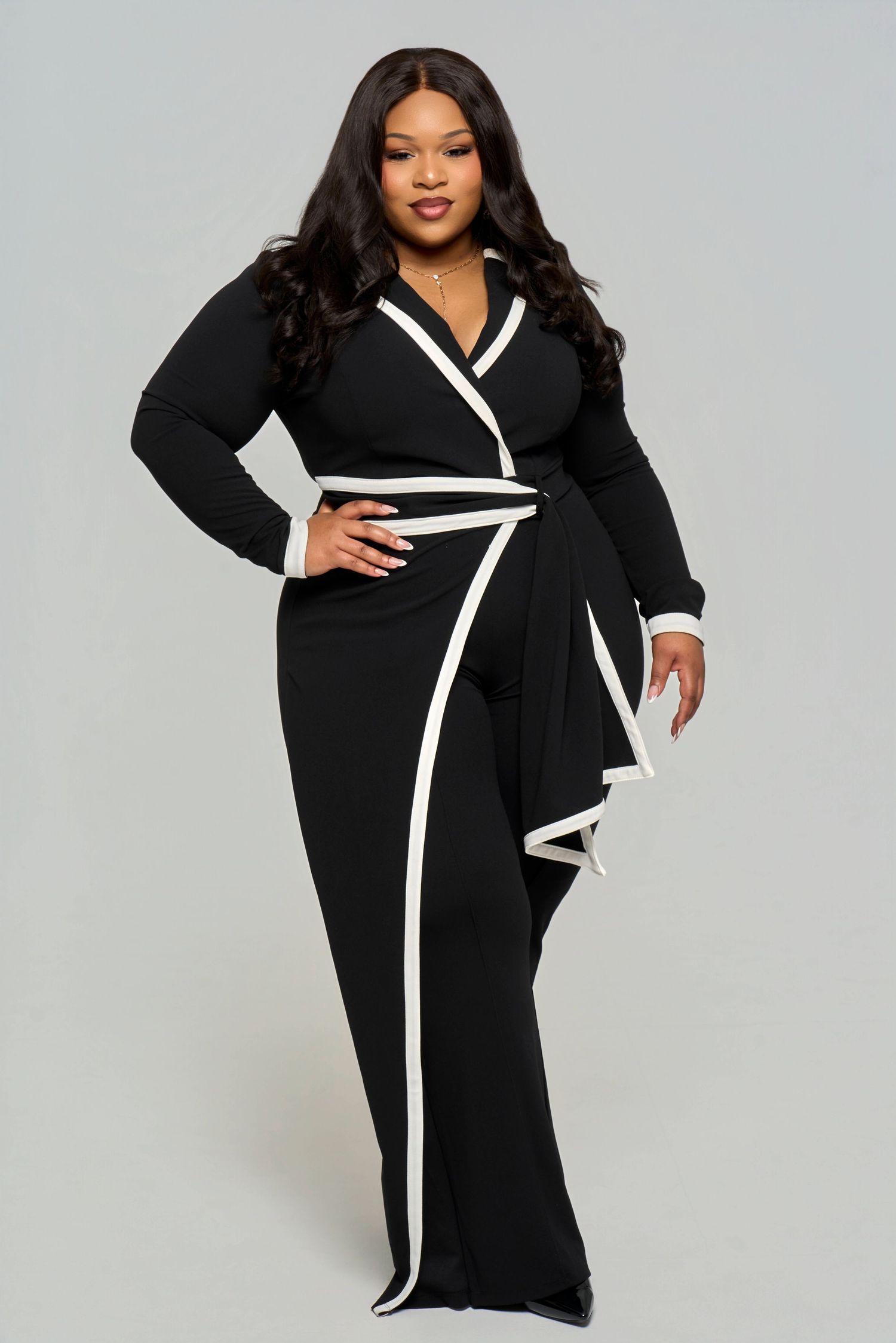 Fashion model wearing black dress with white trim poses elegantly against grey background.