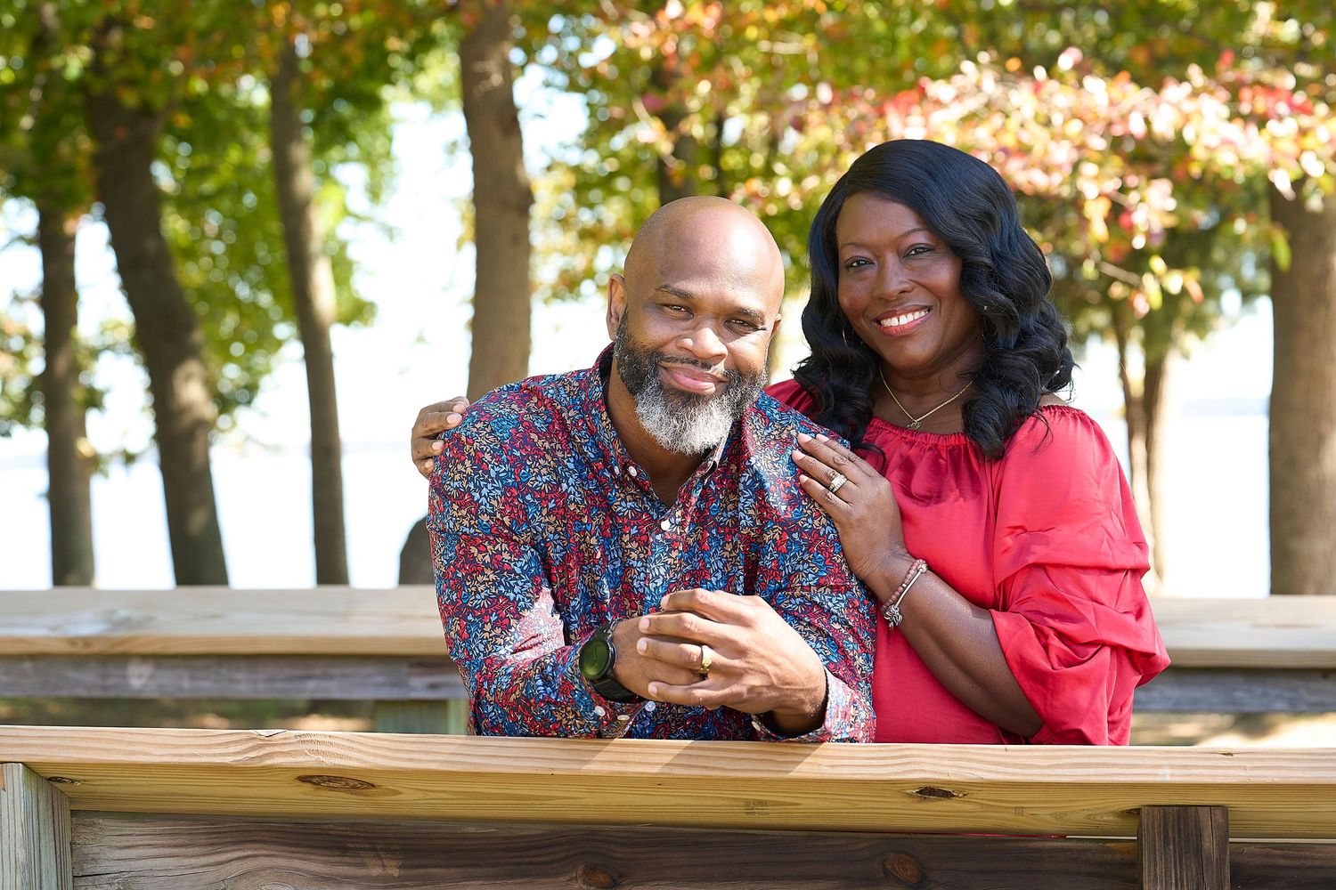 Couple enjoying a romantic moment together on a wooden bench in a park setting with autumn trees in background.