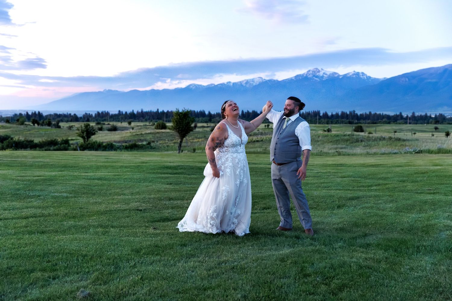A couple celebrates at dusk in an open field with mountains and forest in the background.