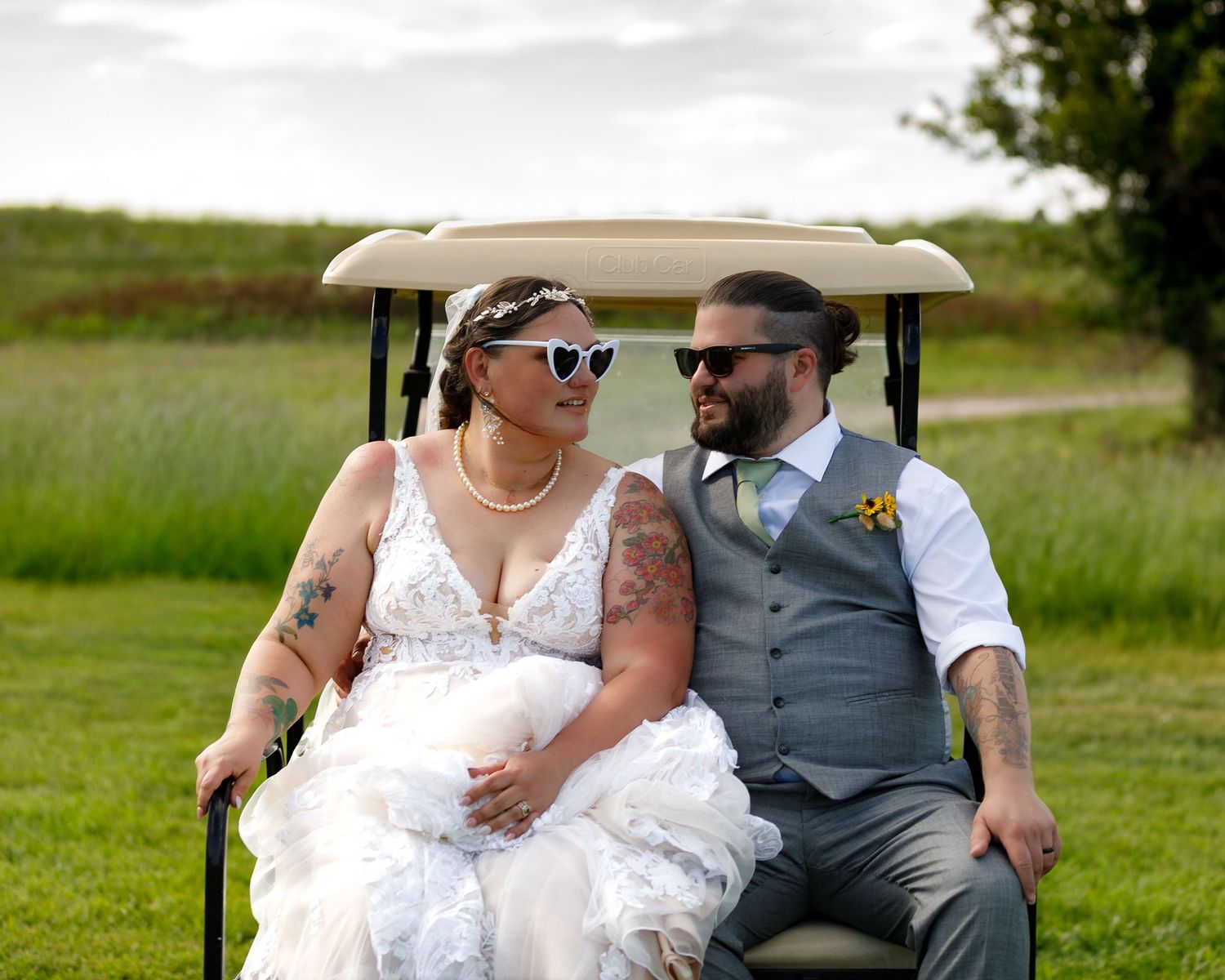 Couple riding together on a golf cart during their wedding celebration in a scenic outdoor setting.
