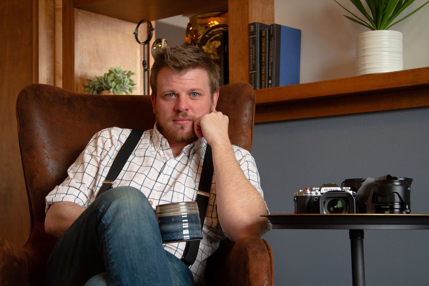 Person sitting on brown leather couch in modern living room with houseplants and natural lighting.