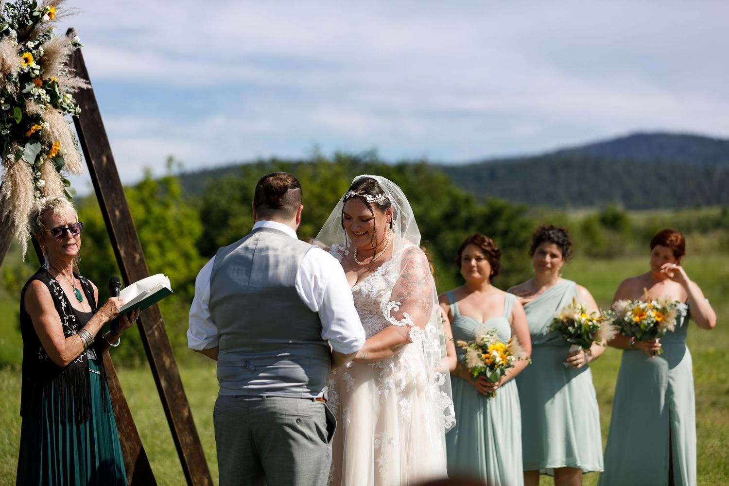 Wedding party gathered outdoors for ceremony with mountains and blue sky in scenic natural background.