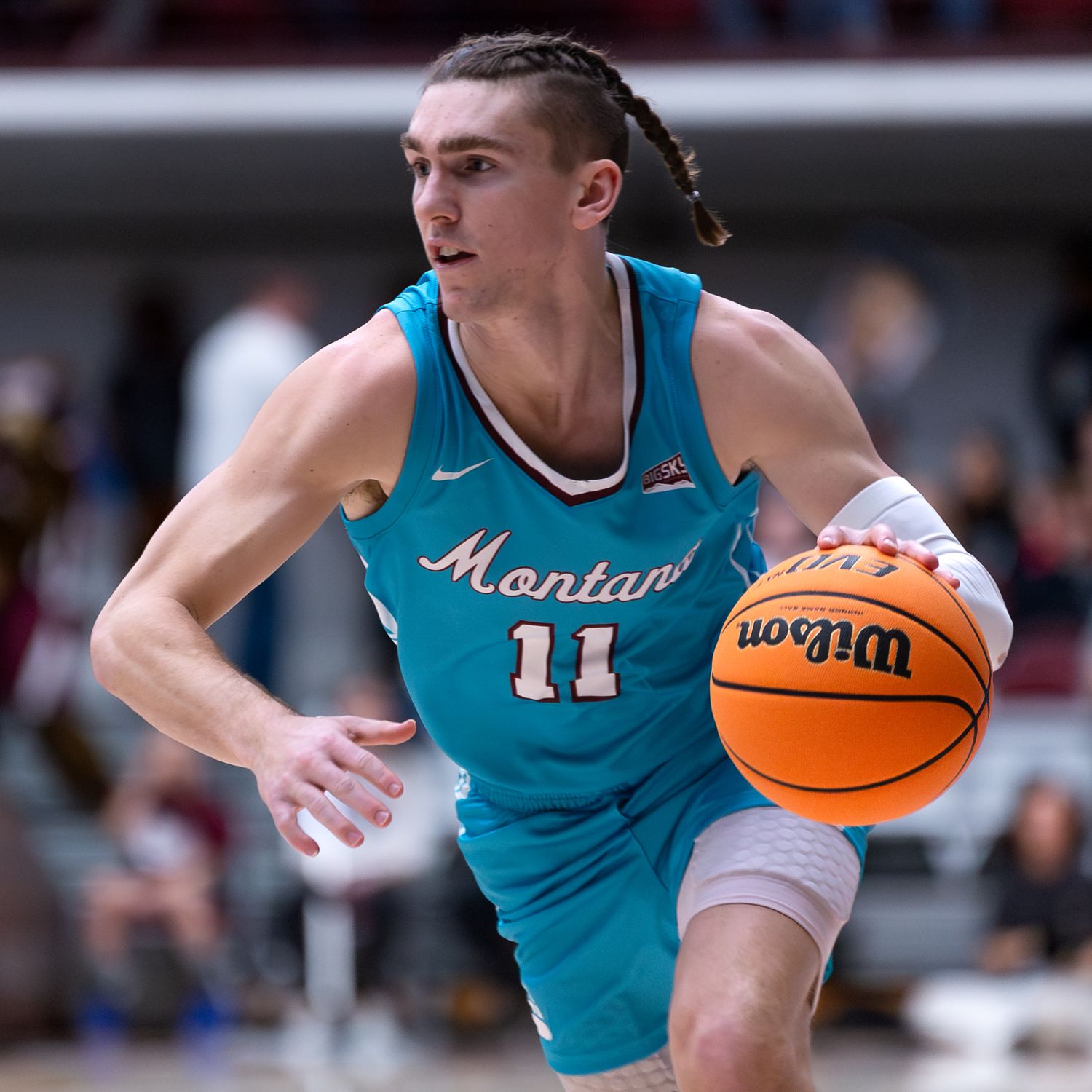 Basketball player in turquoise Montana jersey dribbles while scanning the court.