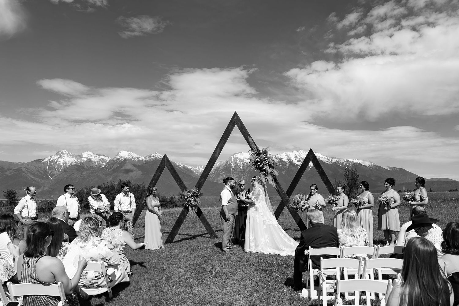 Outdoor mountain wedding ceremony with triangular wooden arches set against a dramatic mountain backdrop in black and white.