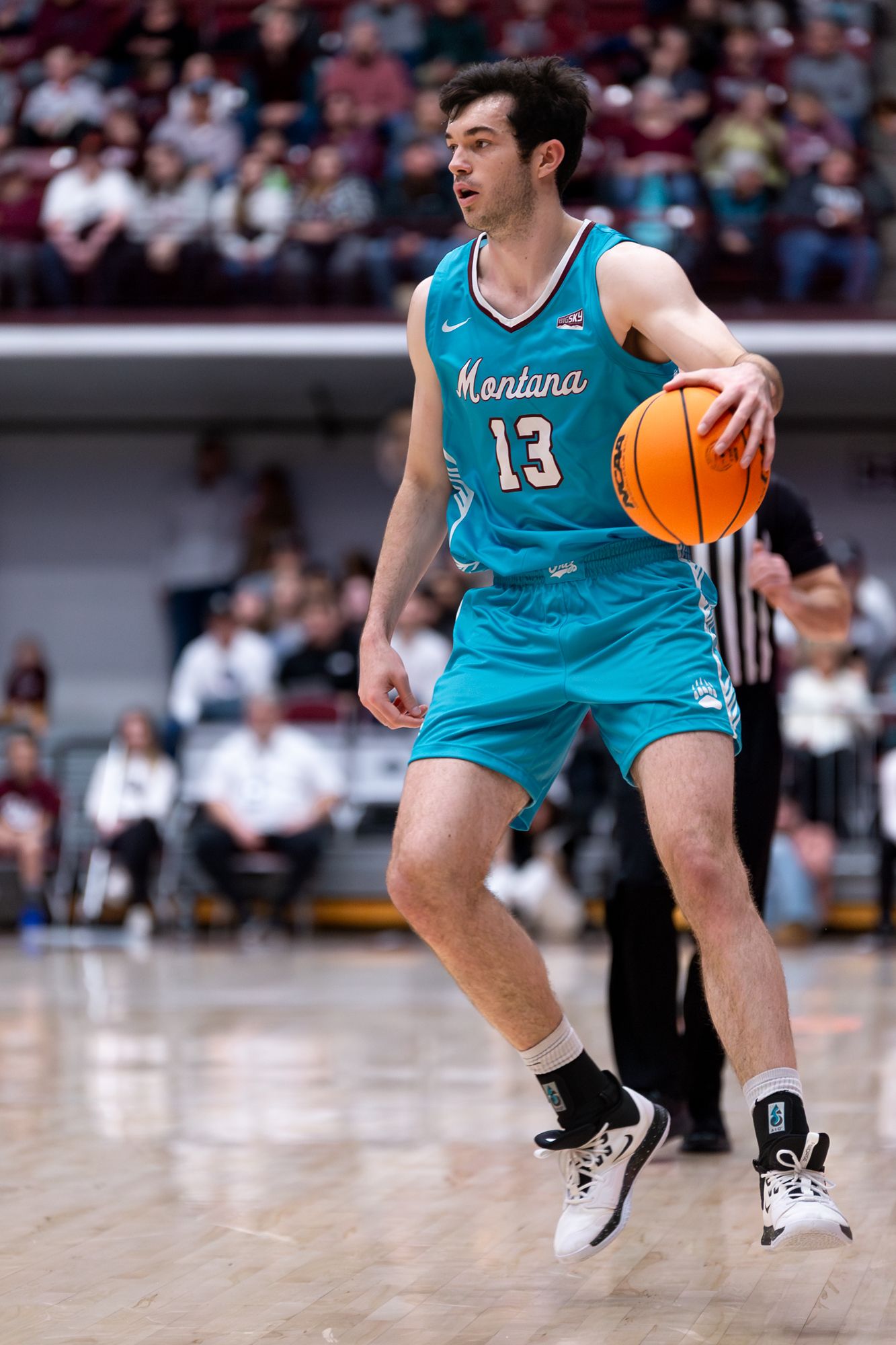 Basketball player in turquoise Montana jersey controls the ball during game.