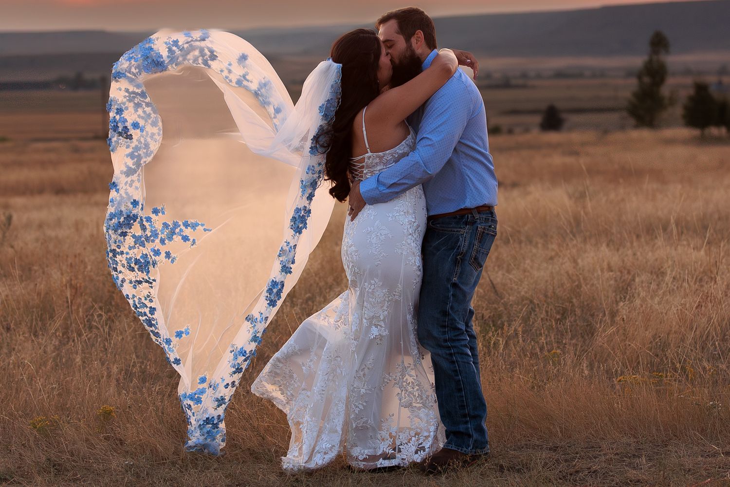 A couple embraces in a golden field at sunset as a lace veil billows dramatically in the wind.