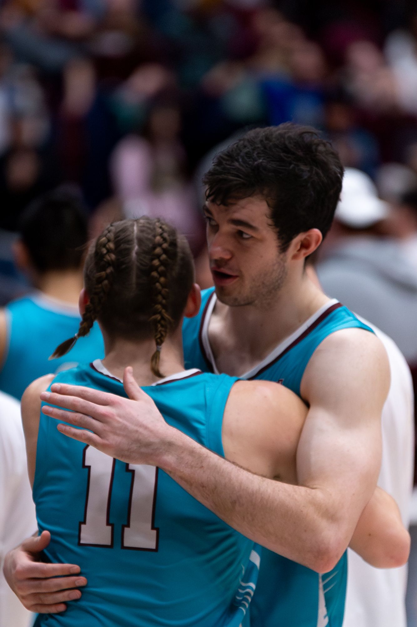 Two basketball players in turquoise jerseys share a supportive moment during the game.