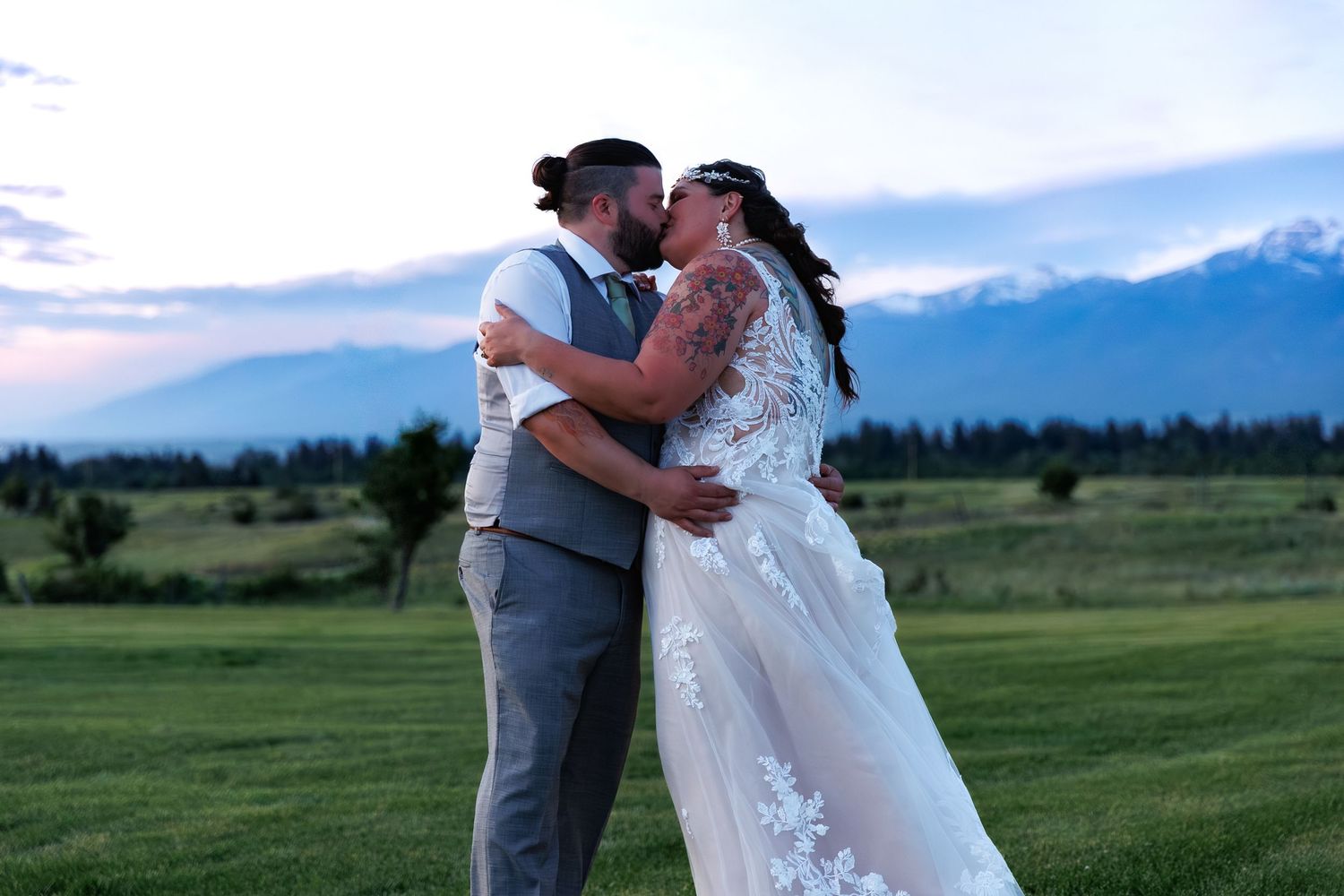 A romantic wedding couple shares a tender kiss in a scenic mountain meadow at sunset.