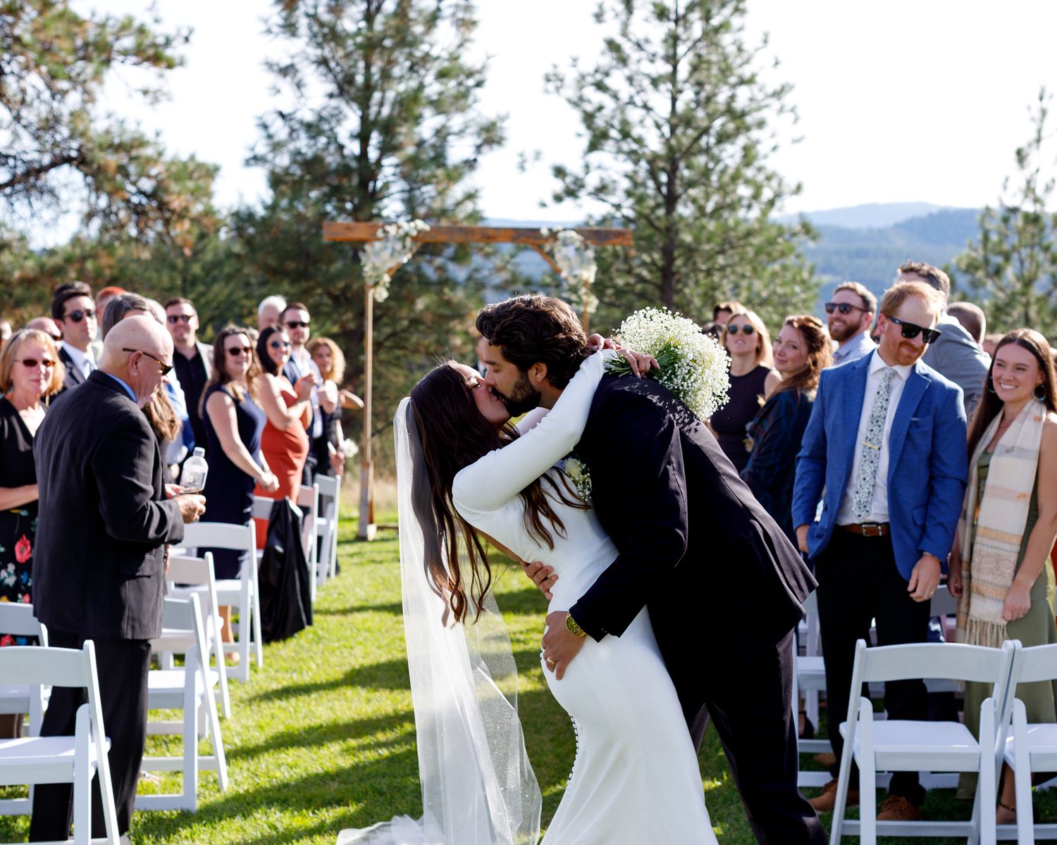 Wedding ceremony on a grassy lawn with white chairs set up and guests standing during the celebration.