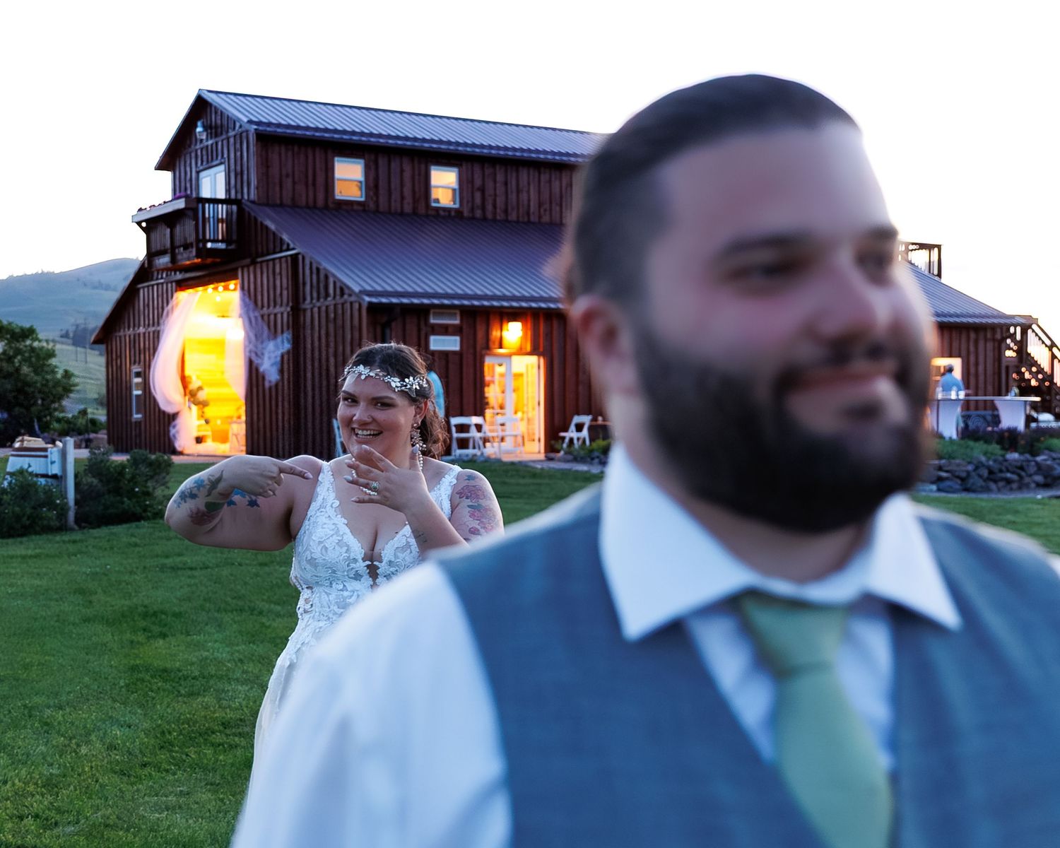 A rustic barn wedding venue at dusk with warm glowing lights and a couple standing on the lawn.