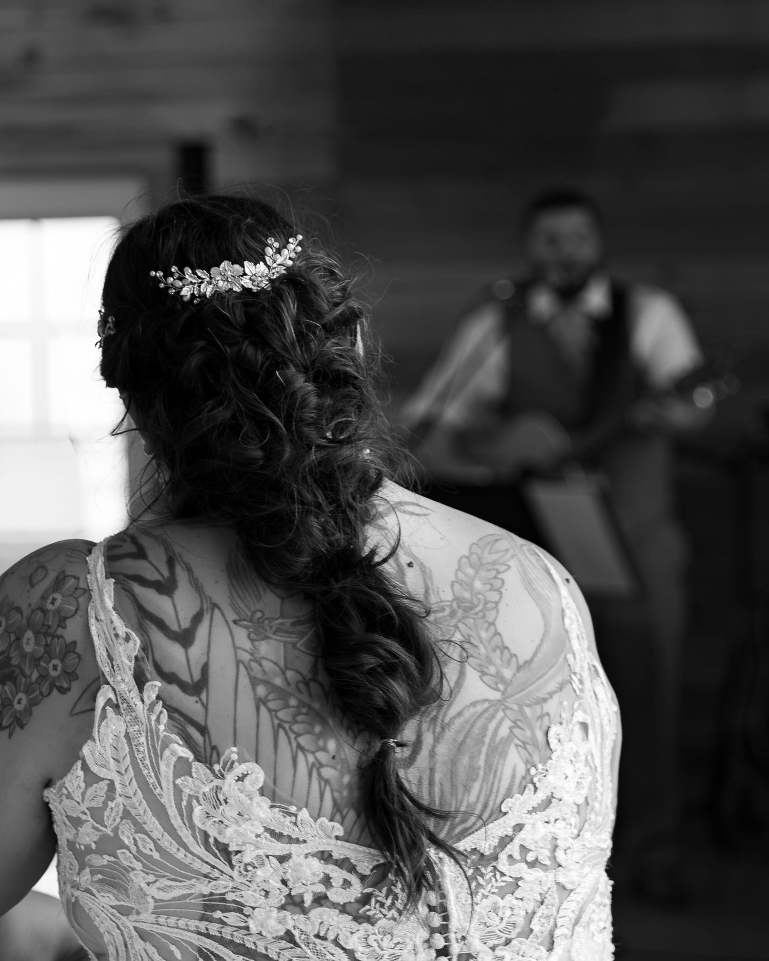 A black and white close-up of a bride's lace wedding dress details and hairstyle from behind.