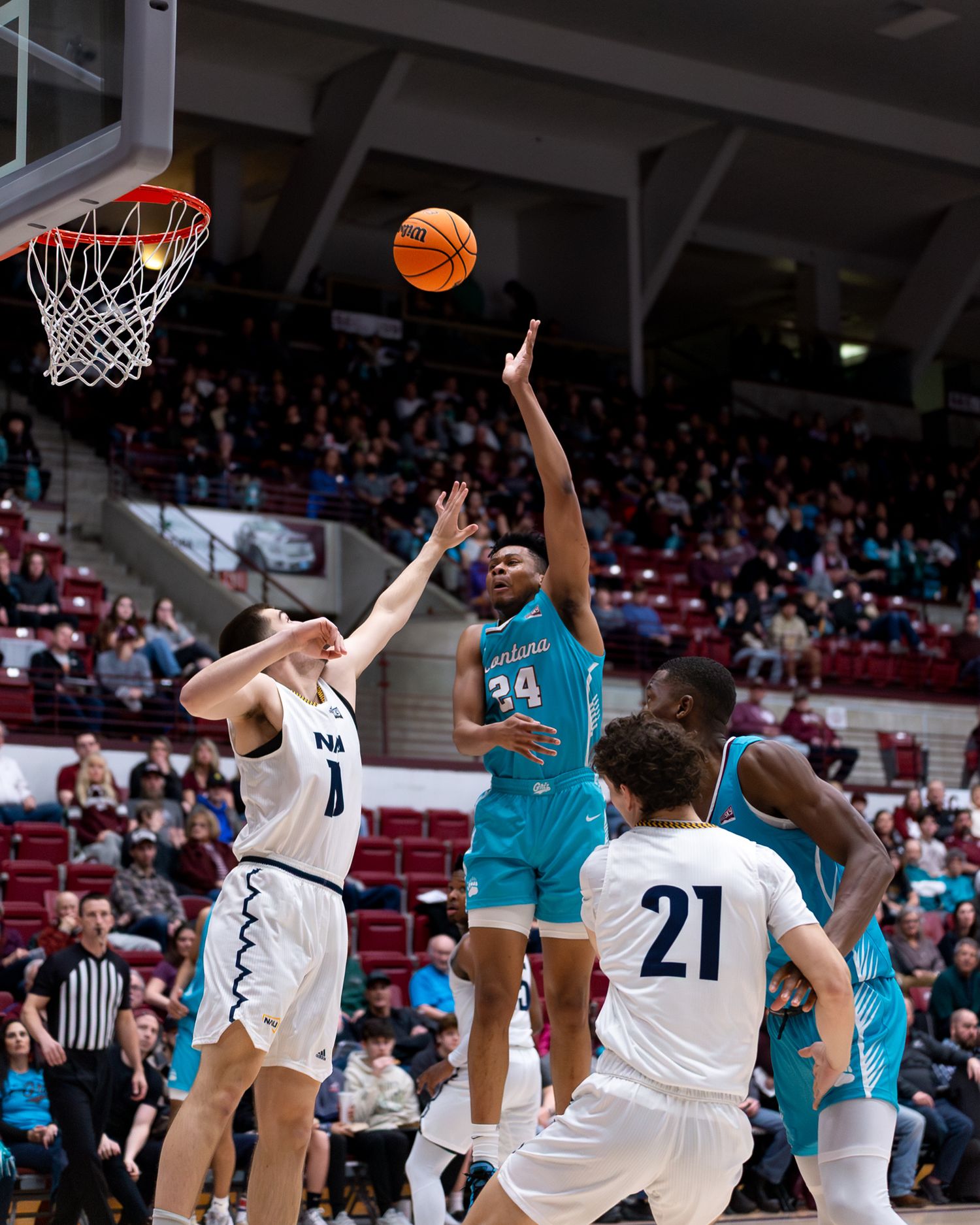 Basketball player takes jump shot while being defended by two opponents in white jerseys.
