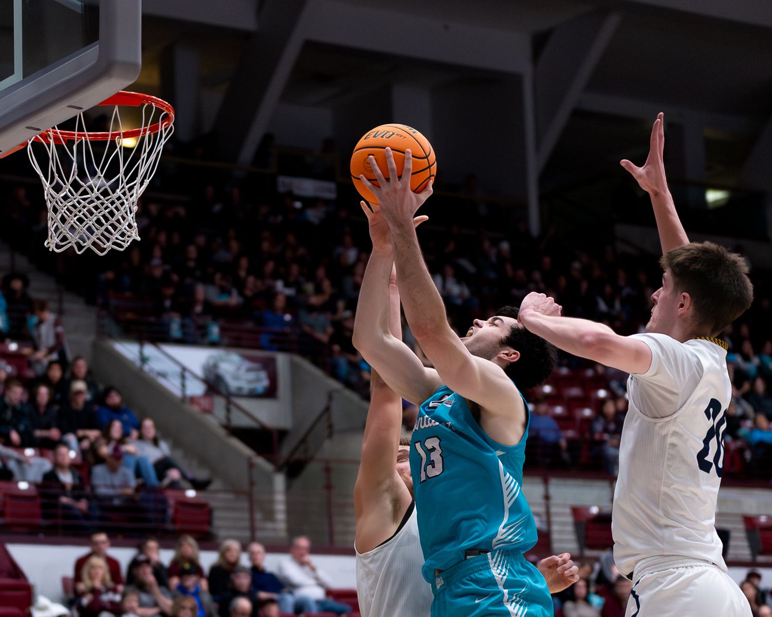 Basketball player attempts a shot while being defended by two opponents near the basket.
