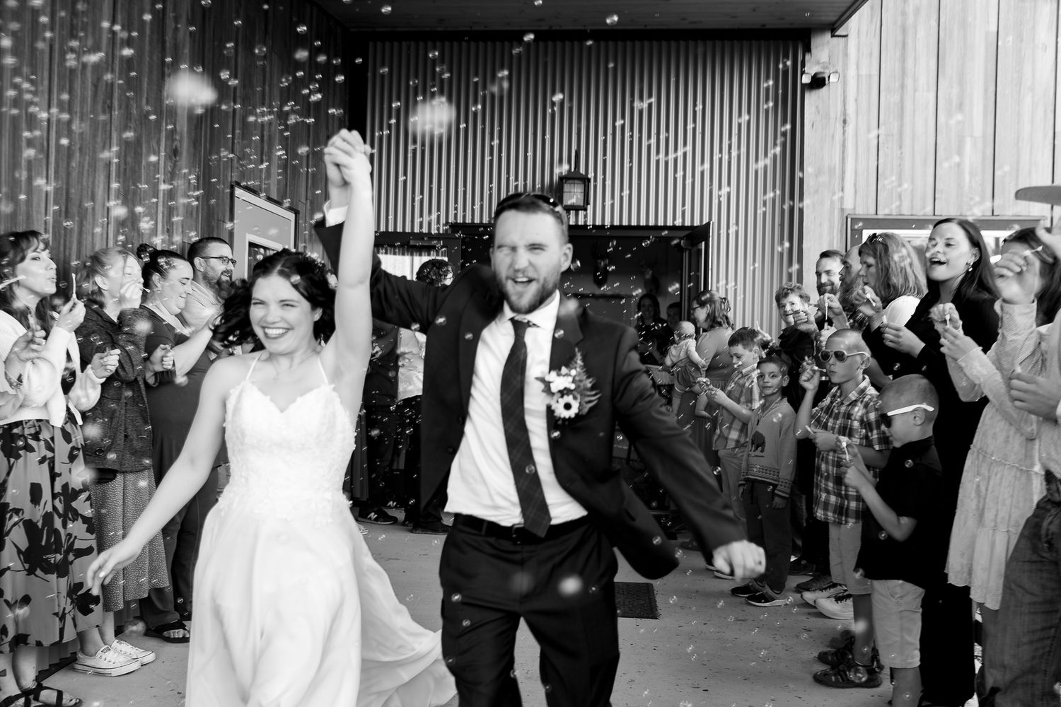 Wedding guests dance and celebrate on a dance floor at a reception while raising their arms in joyful celebration.