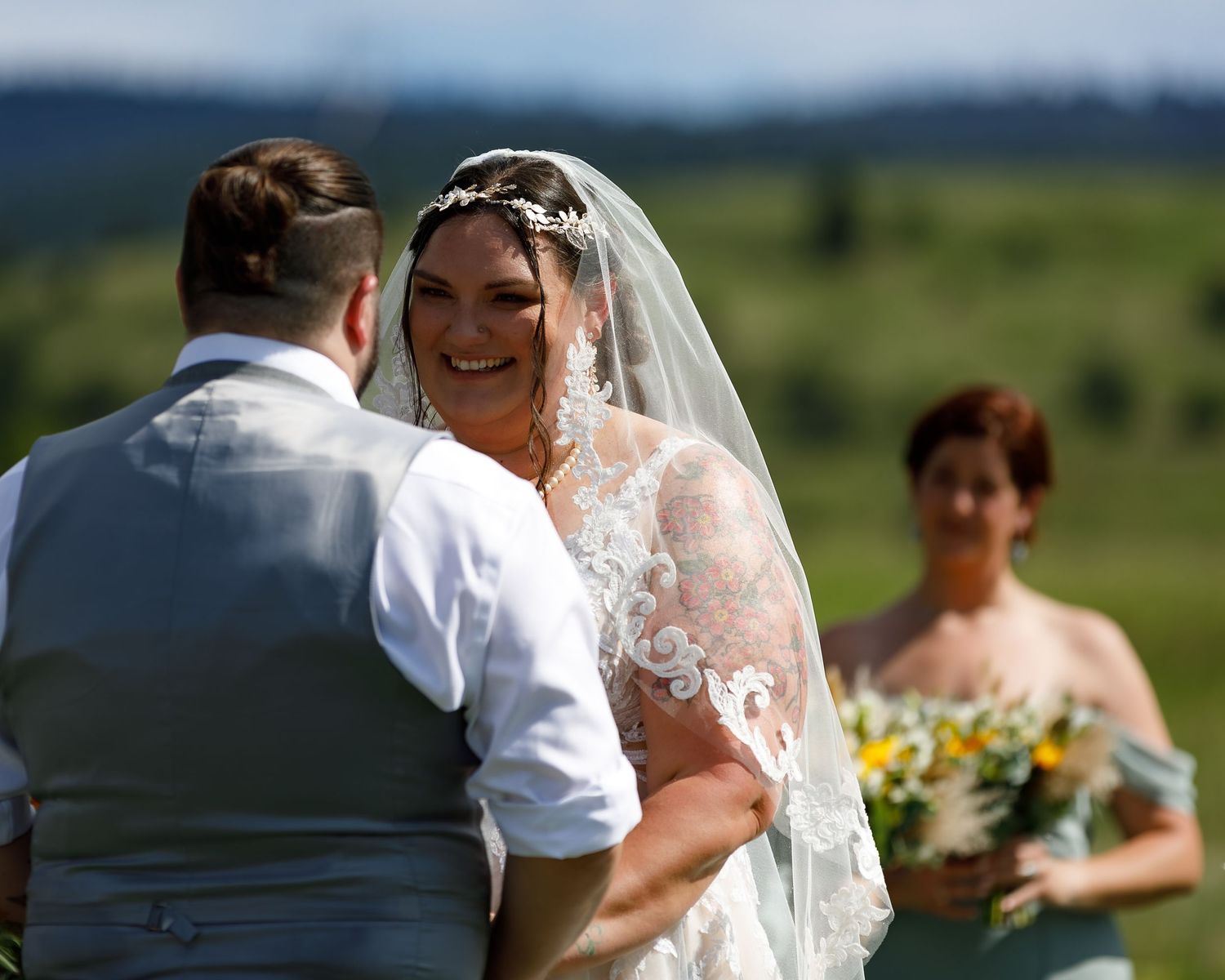 A joyful outdoor wedding ceremony with rolling hills in the background on a sunny summer day.