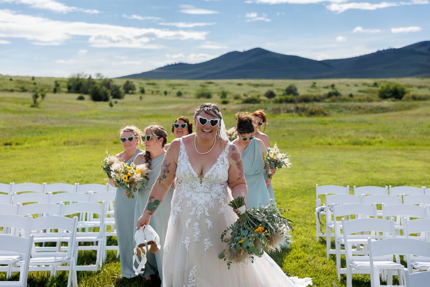 Outdoor wedding ceremony setup with white chairs on green rolling hills against a backdrop of mountains and blue sky.