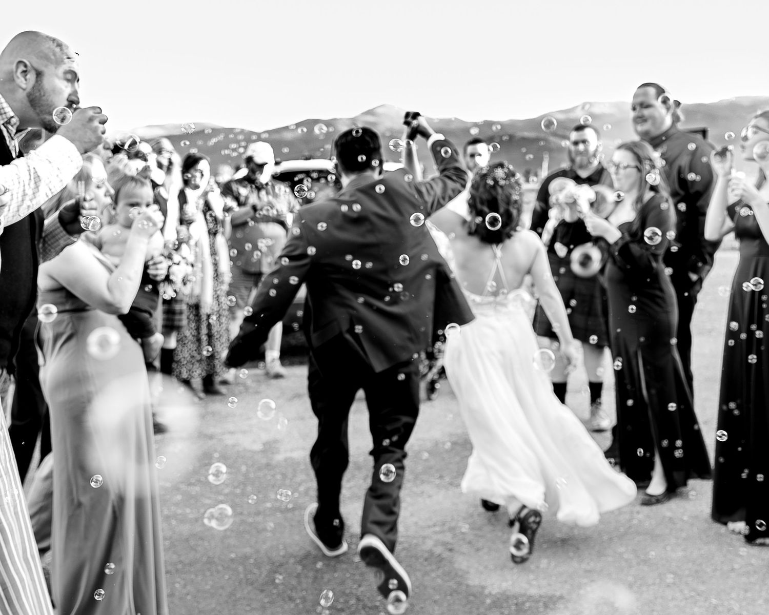Wedding party members dance and celebrate outdoors during a joyful reception celebration.