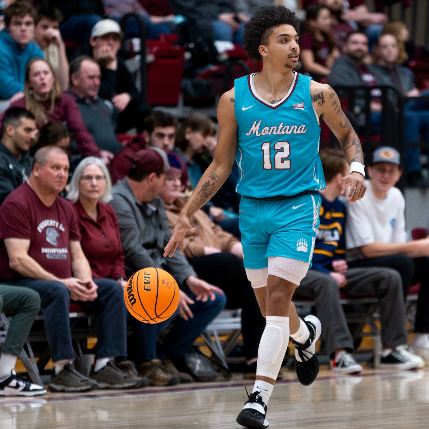 Basketball player in turquoise Montana jersey dribbles ball during competitive game.