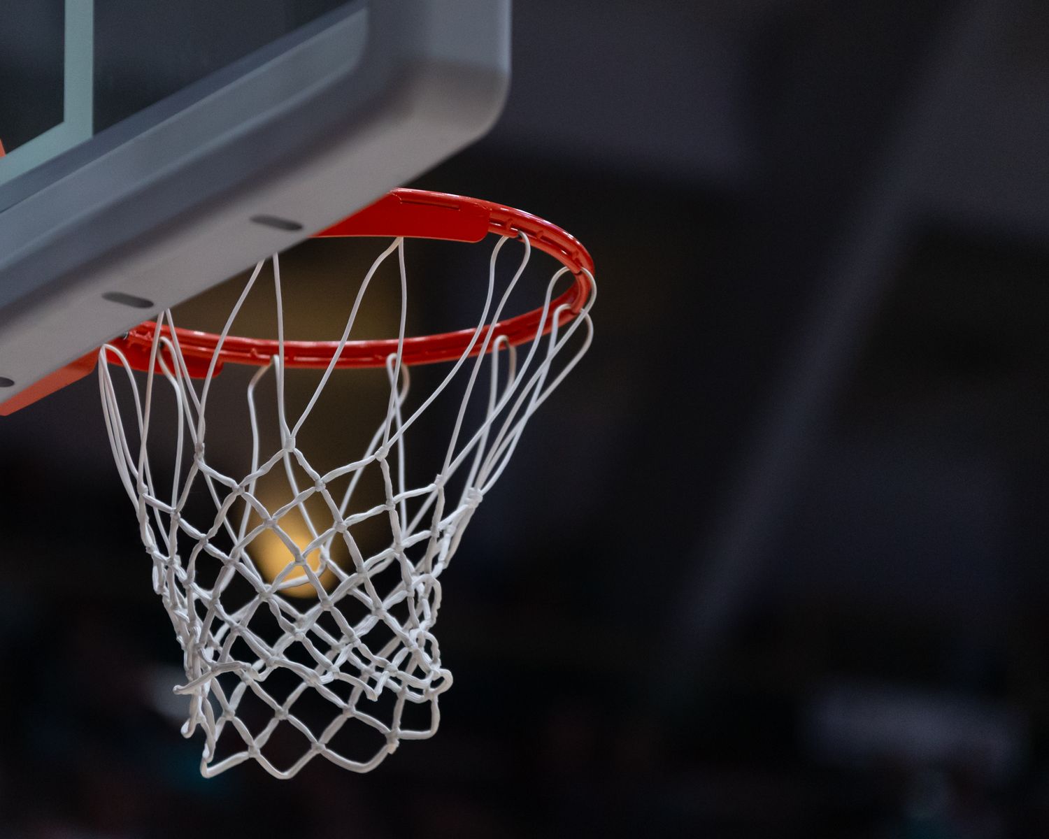 Basketball sinking through the net against a dark background during a game.