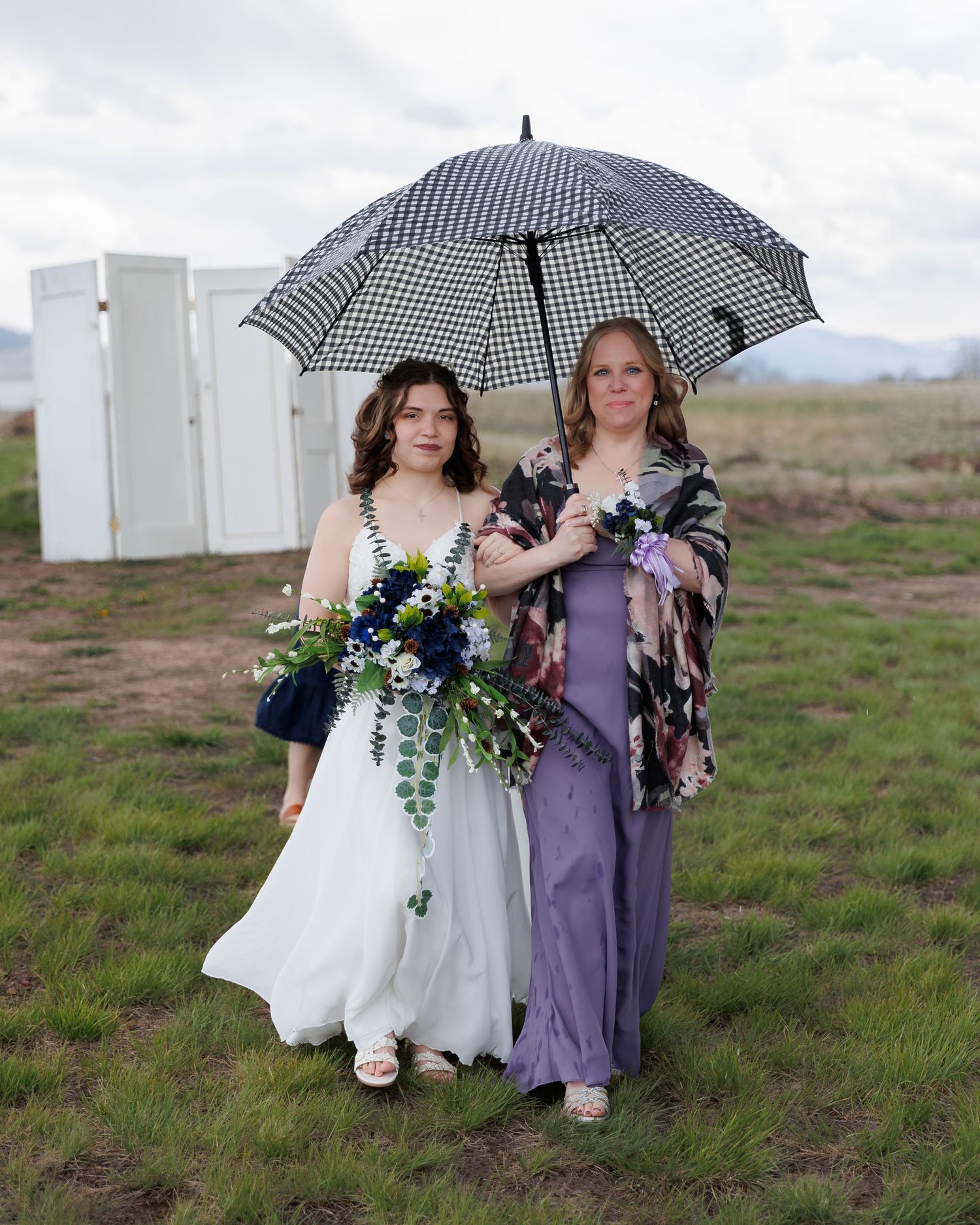 Two figures holding umbrellas stand together in a grassy field on an overcast day.