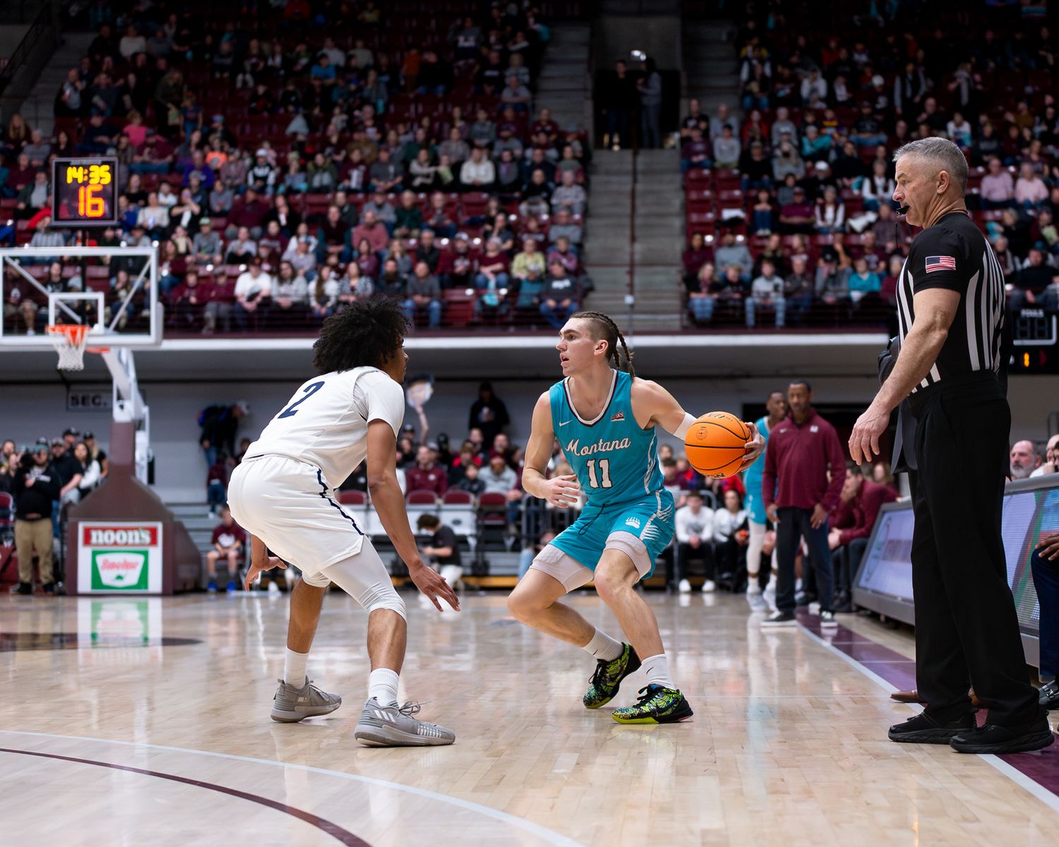 Basketball players compete on the court with a referee observing the play.