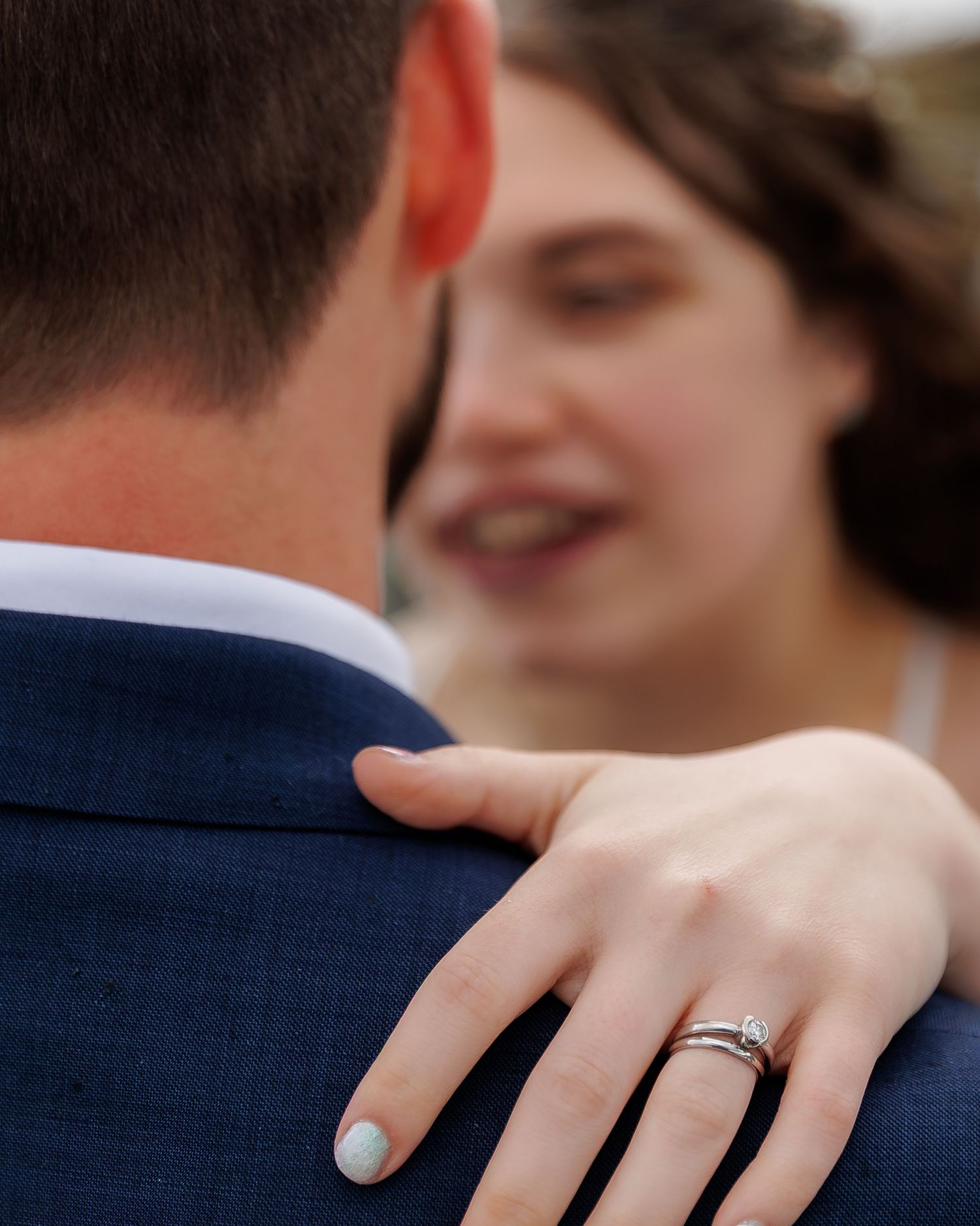 Close-up shot of a diamond engagement ring being shown on a hand with light blue nail polish.