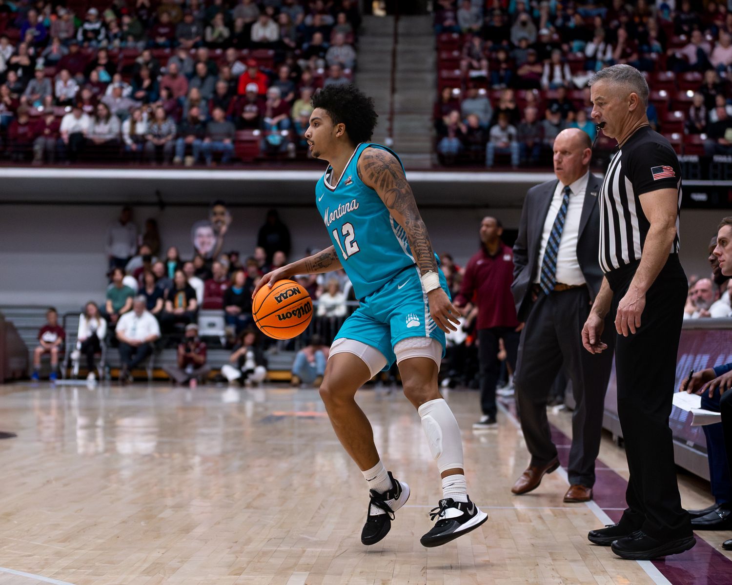 Basketball player in turquoise uniform dribbles near sideline during game.