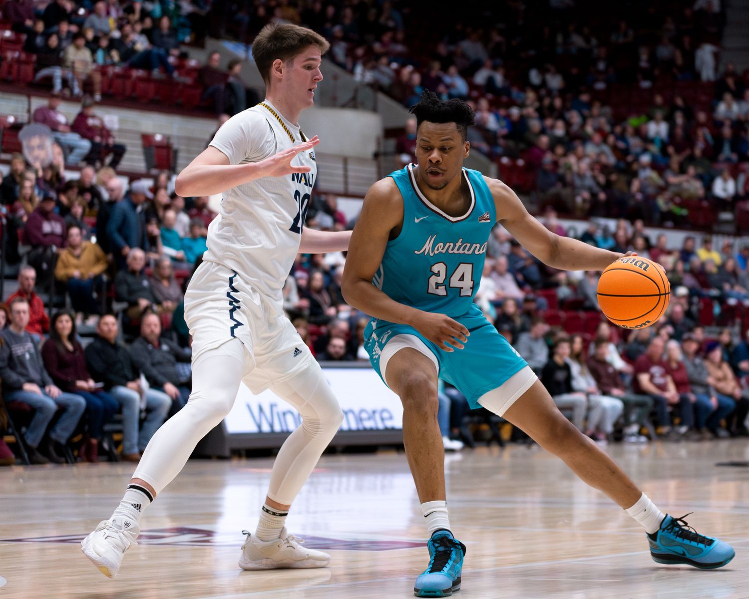 Basketball player in turquoise jersey drives past defender in white uniform.