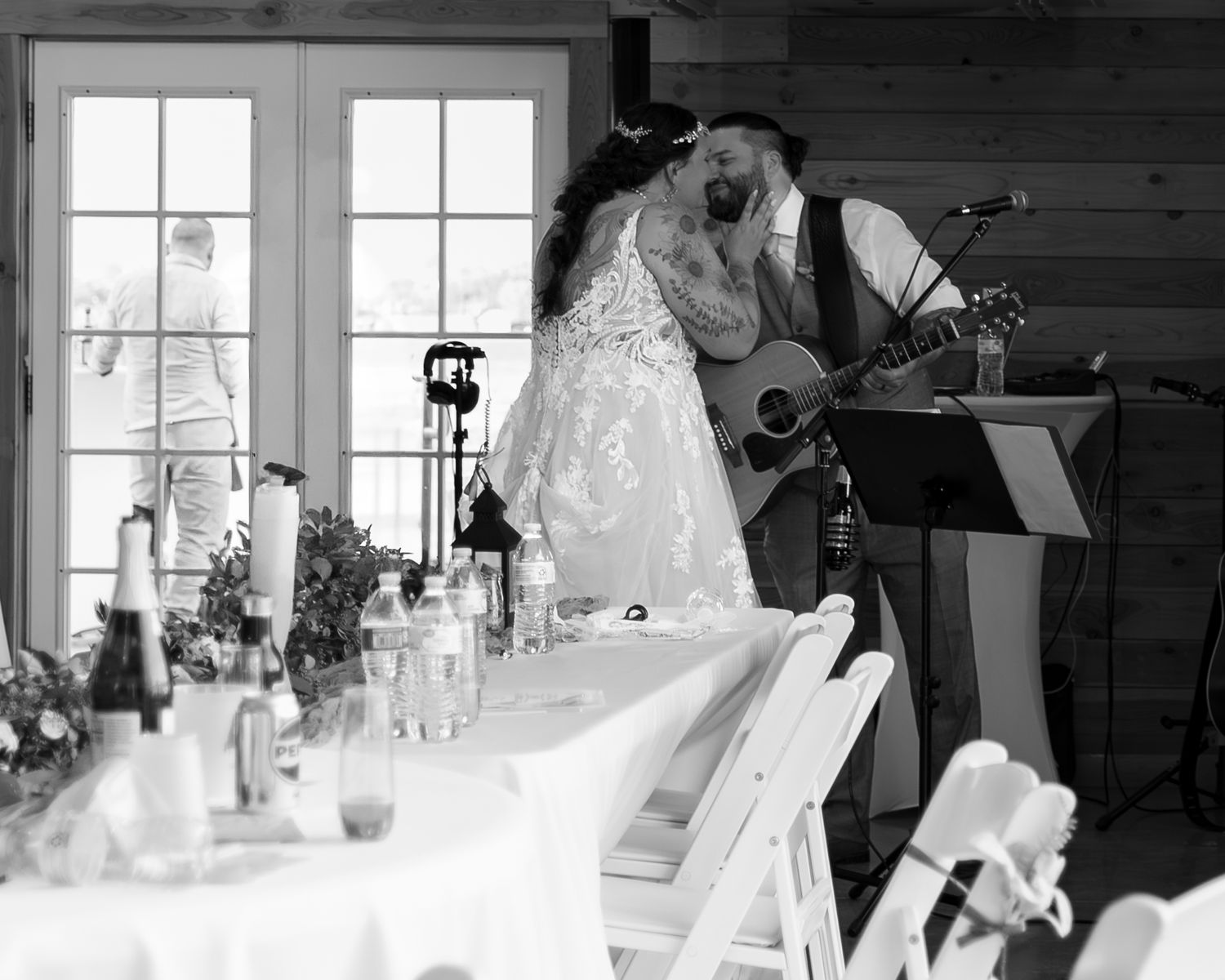 A rustic wedding reception venue with white tablecloths and natural wood walls illuminated by large windows.