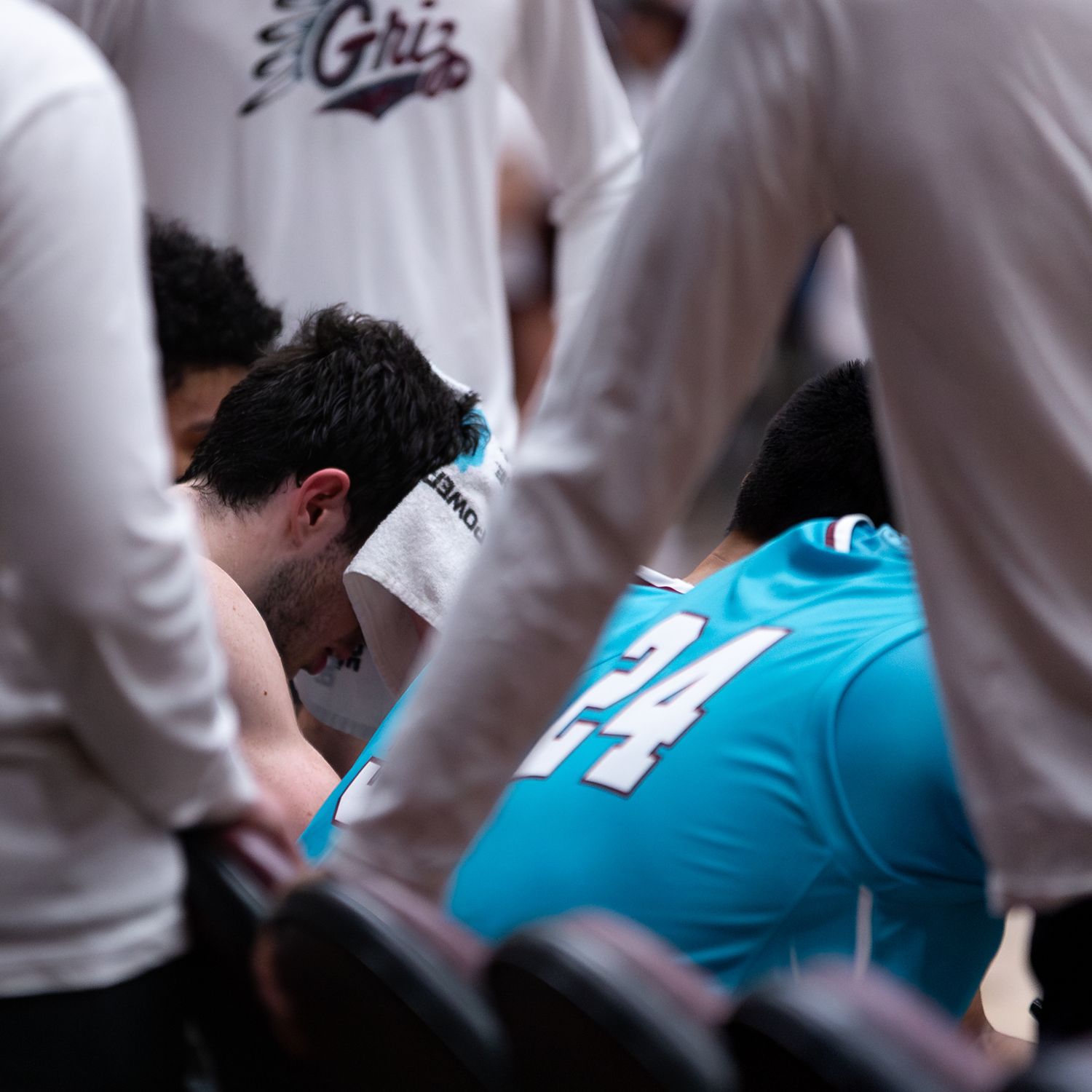 Basketball team huddles during a timeout with players in white jerseys and one in turquoise.