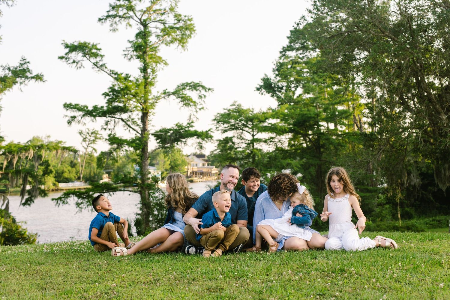 Group of people sitting together on grassy slope in park with tall trees in background on sunny day.