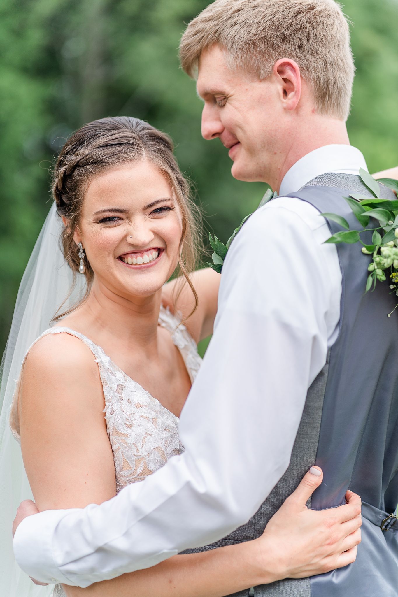 A couple shares a tender moment outdoors with greenery in the background.