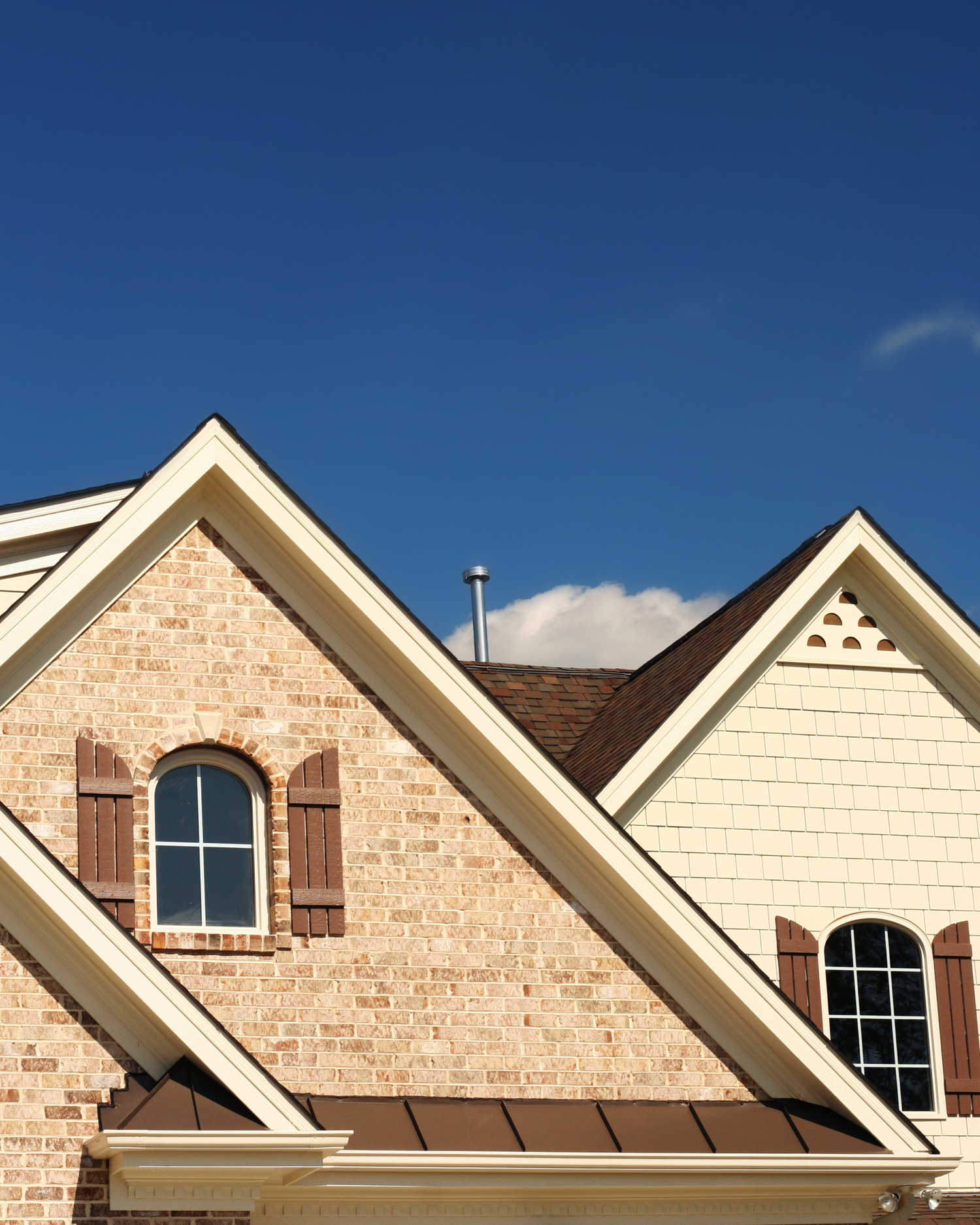 Row of beige stone residential rooflines with gabled peaks and arched windows against a bright blue sky.