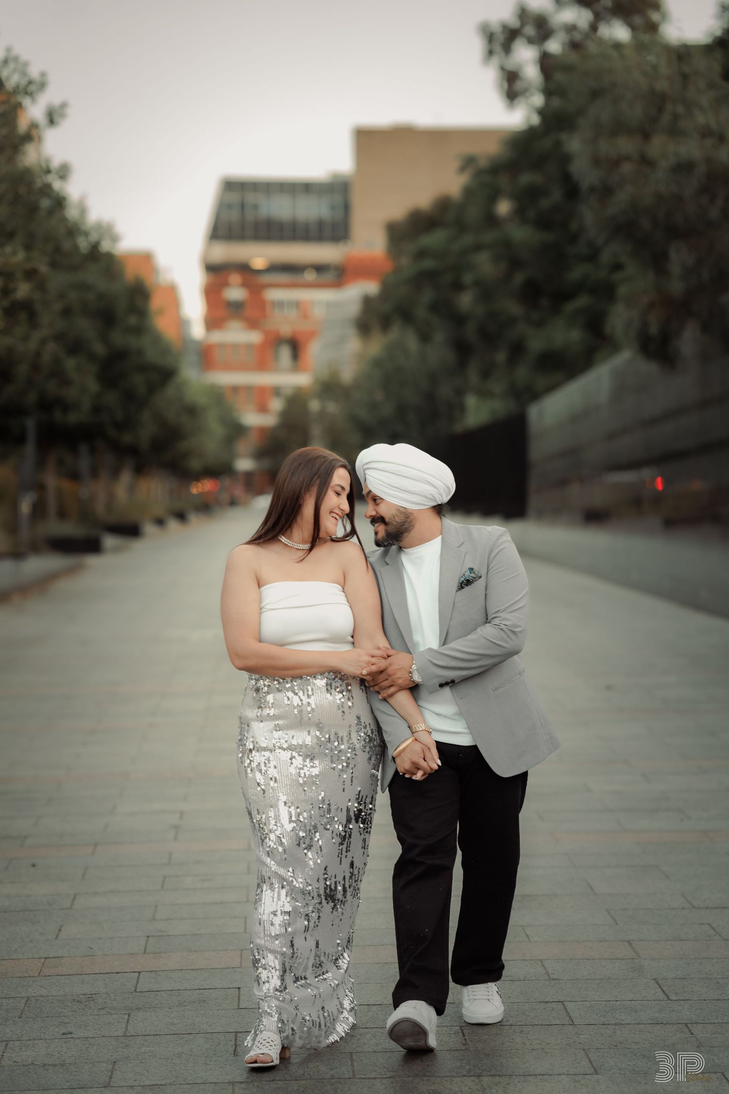 A couple in wedding attire shares an intimate moment while walking along a stone path at dusk.